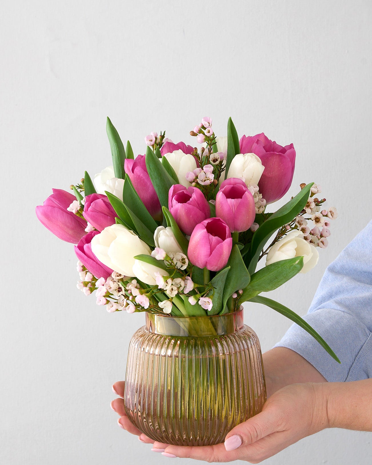 Woman holding soft pink ribbed vase with pink and what tulips with white waxflowers