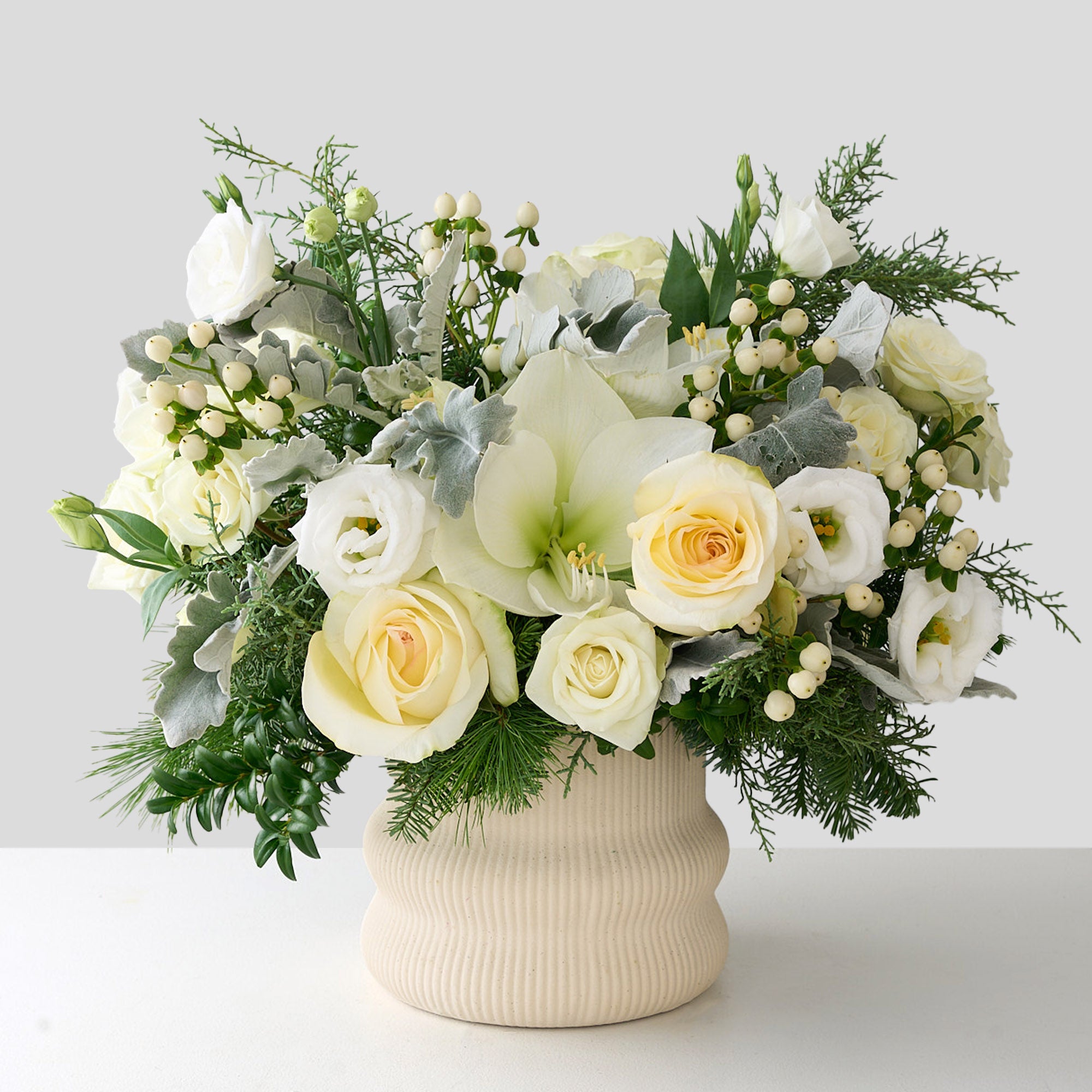 Christmas flower arrangement with white cymbidium orchid, white roses, lianthus, hypericum with silver green leaves, boxwood and other winter greens.