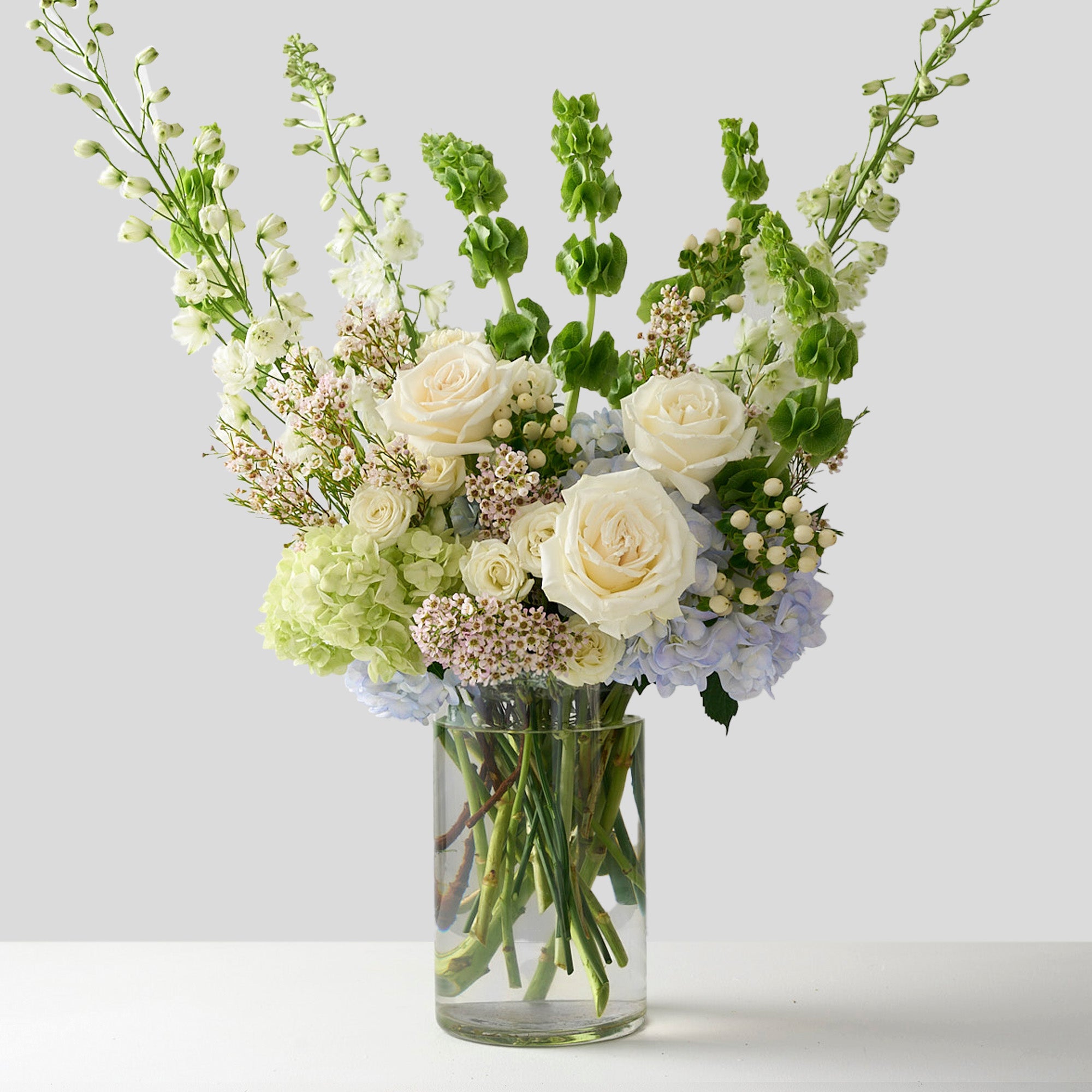 Tall flower arrangement with white delphinium, green bells of Ireland, blue & green hydrangea, white roses