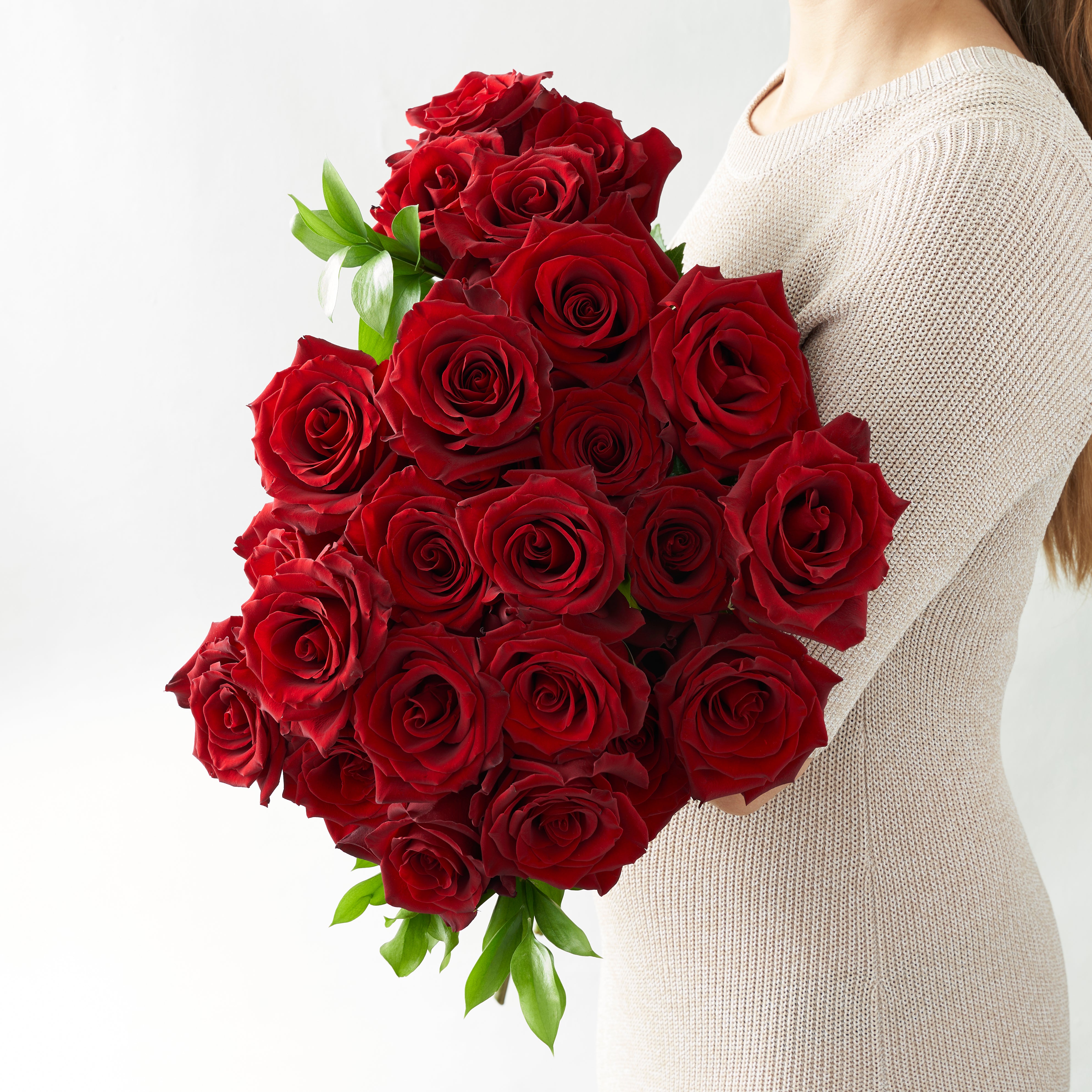 Woman in white top holding a collection of two dozen red roses