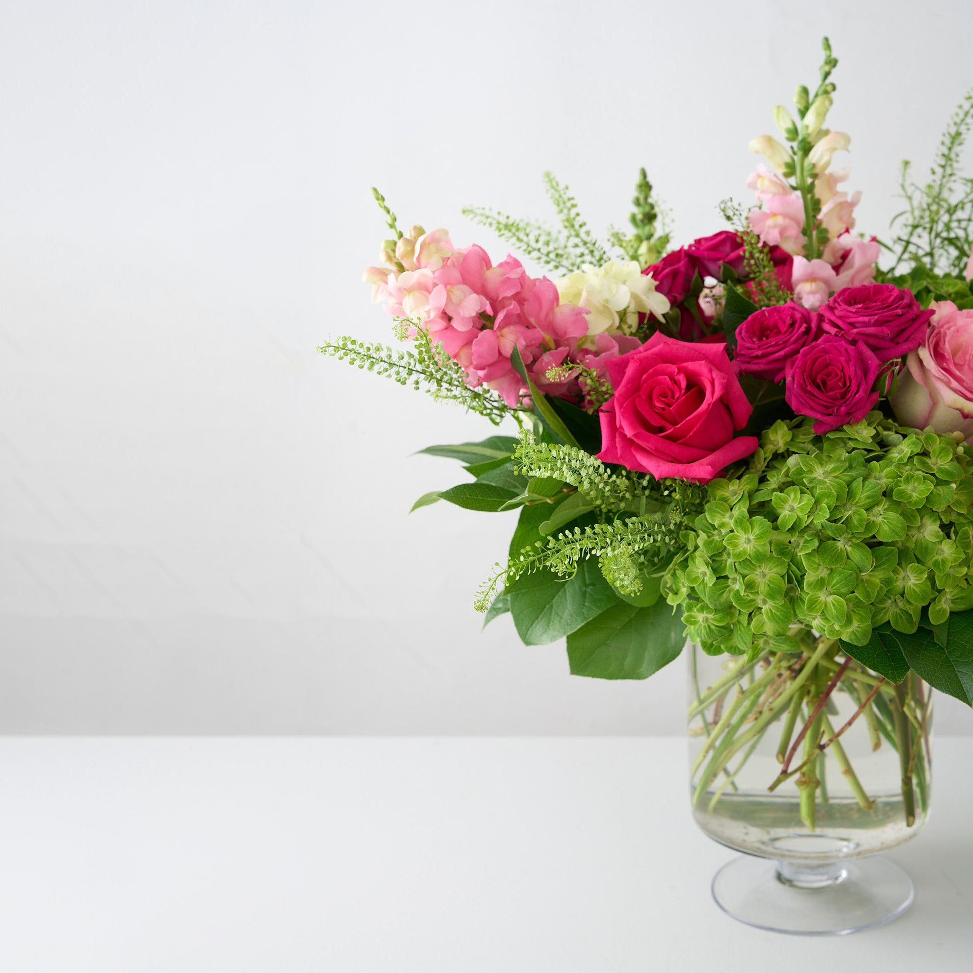 valentine's day arrangement with pink, hot pick roses, snap dragons, and hydrangea in a clear pedestal vase