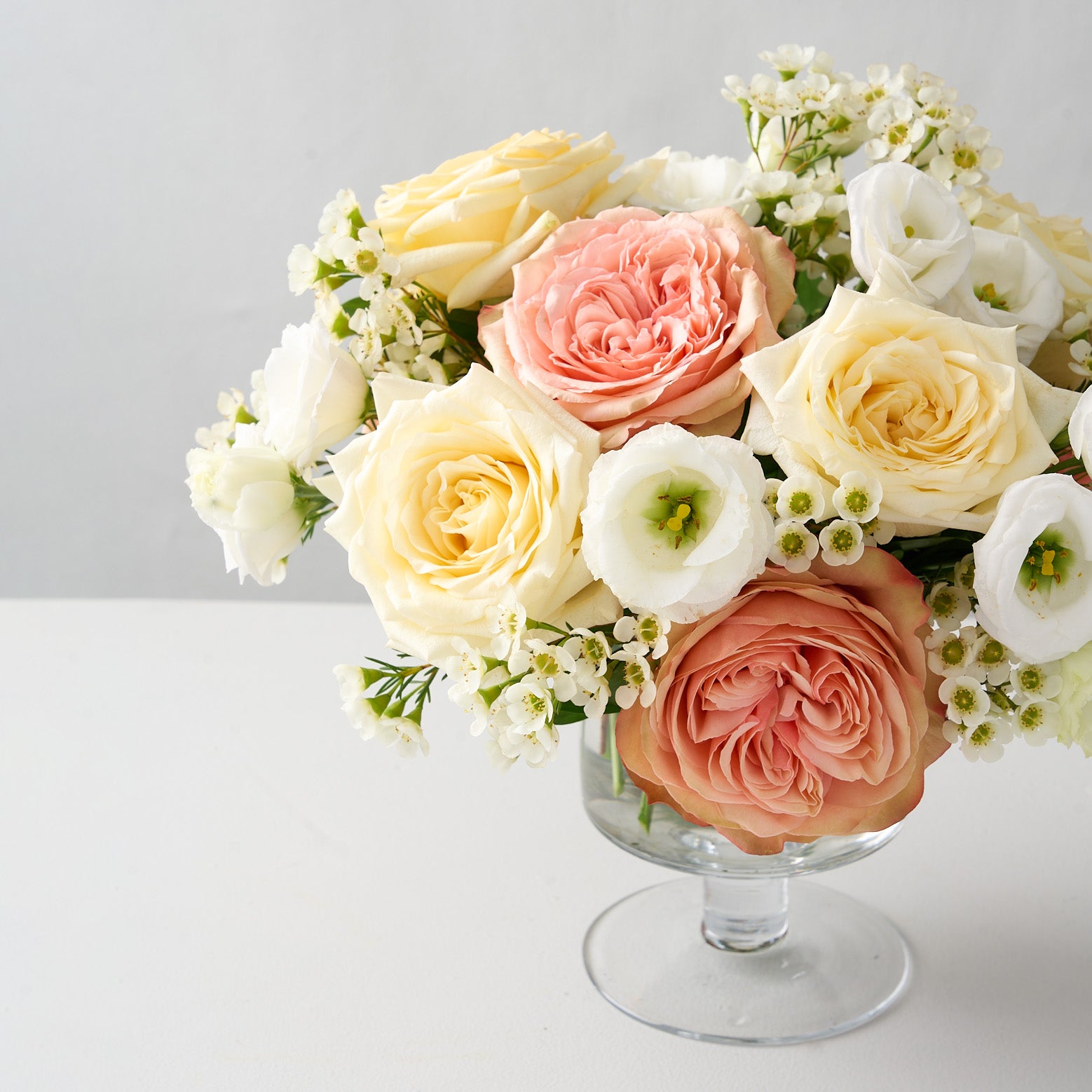 floral arrangement of pink khala and creamy white candlelight roses, white wax flowers and lisanthus in a pedestal glass vase.