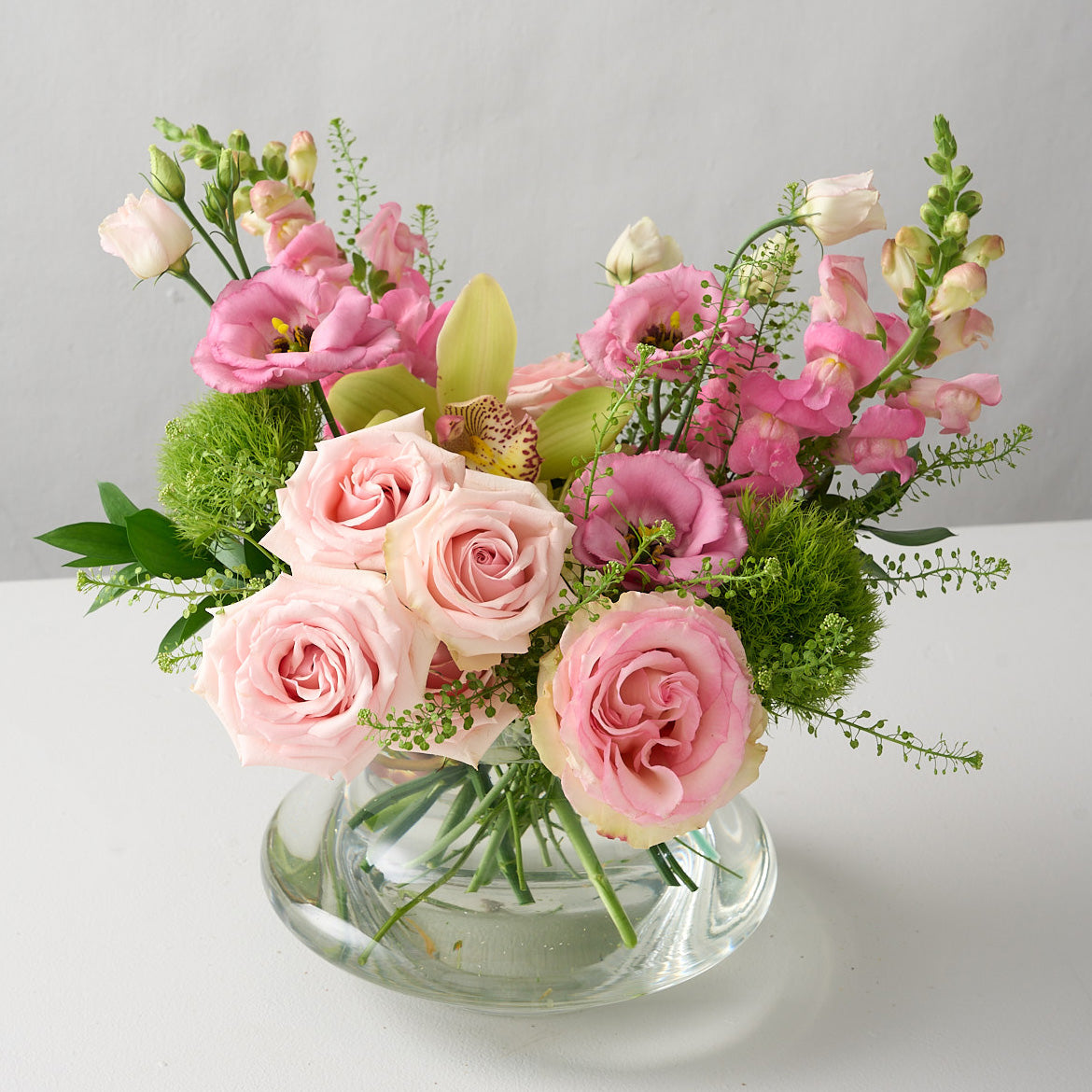 arrangement with pink roses, green trick mums, snap dragons in a low glass genie vase