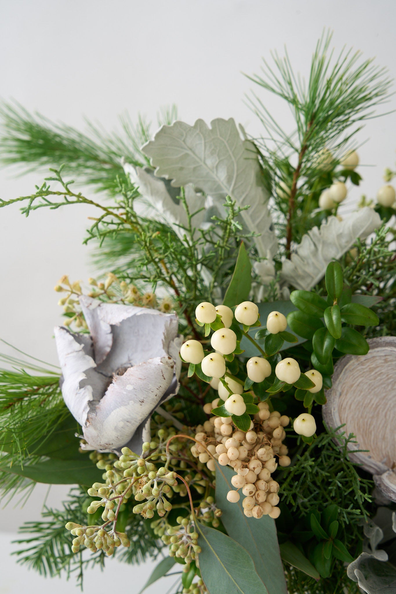 White Pine, cedar, seeded eucalyptus, white hypericum, boxwood in a white deco pot with silver badman pods accents.