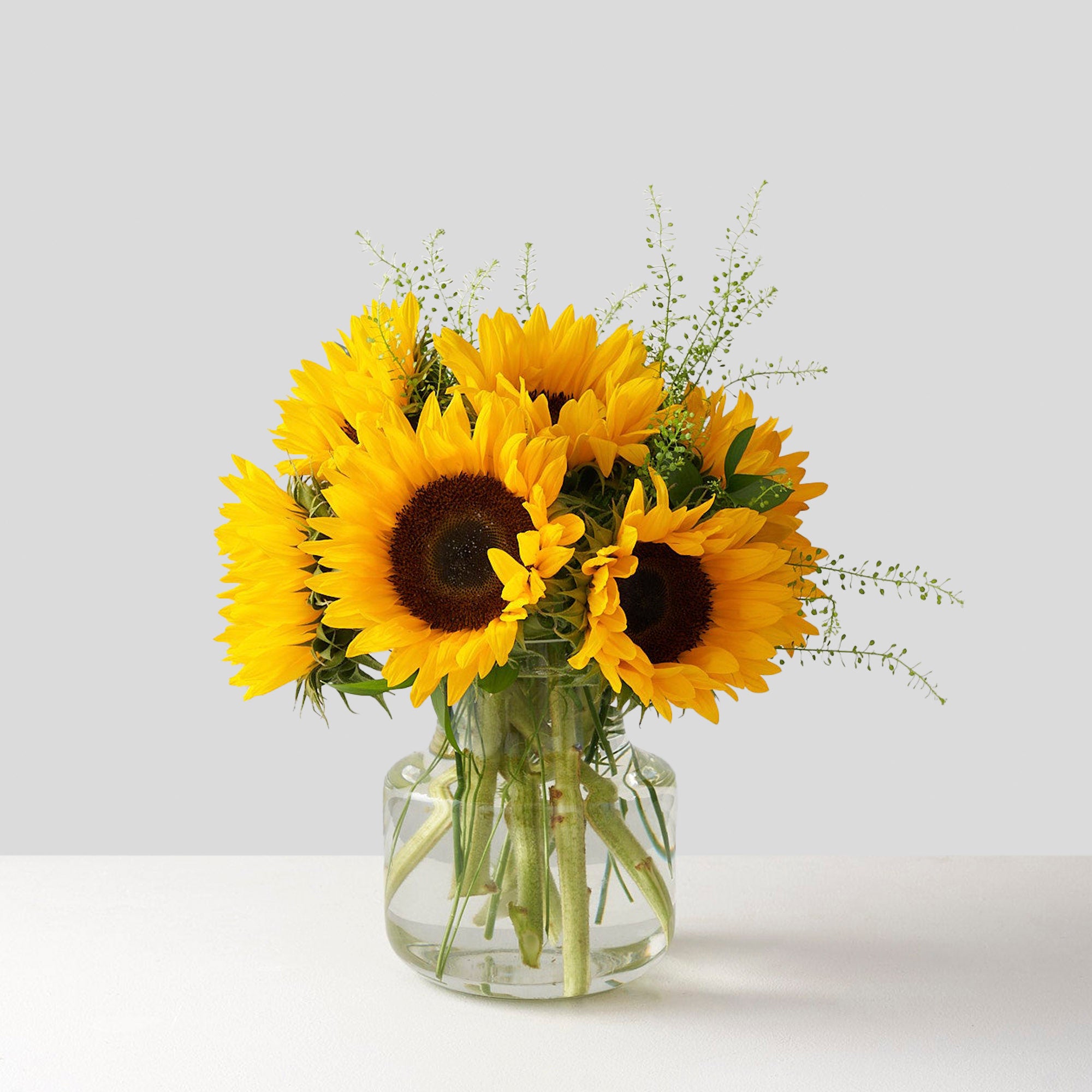 8 yellow sunflowers with brown center in a clear glass vase
