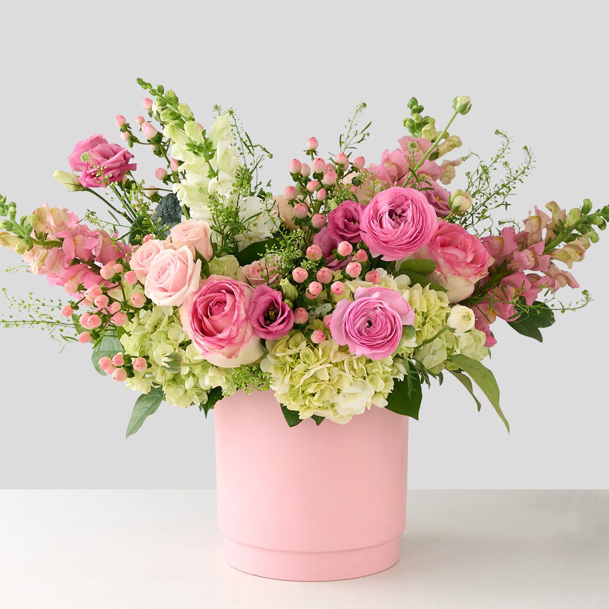 vase arrangement with pink ranunculus, white hydrangea, snapdragons, Esperance roses, and hypericum in a light pink vase.