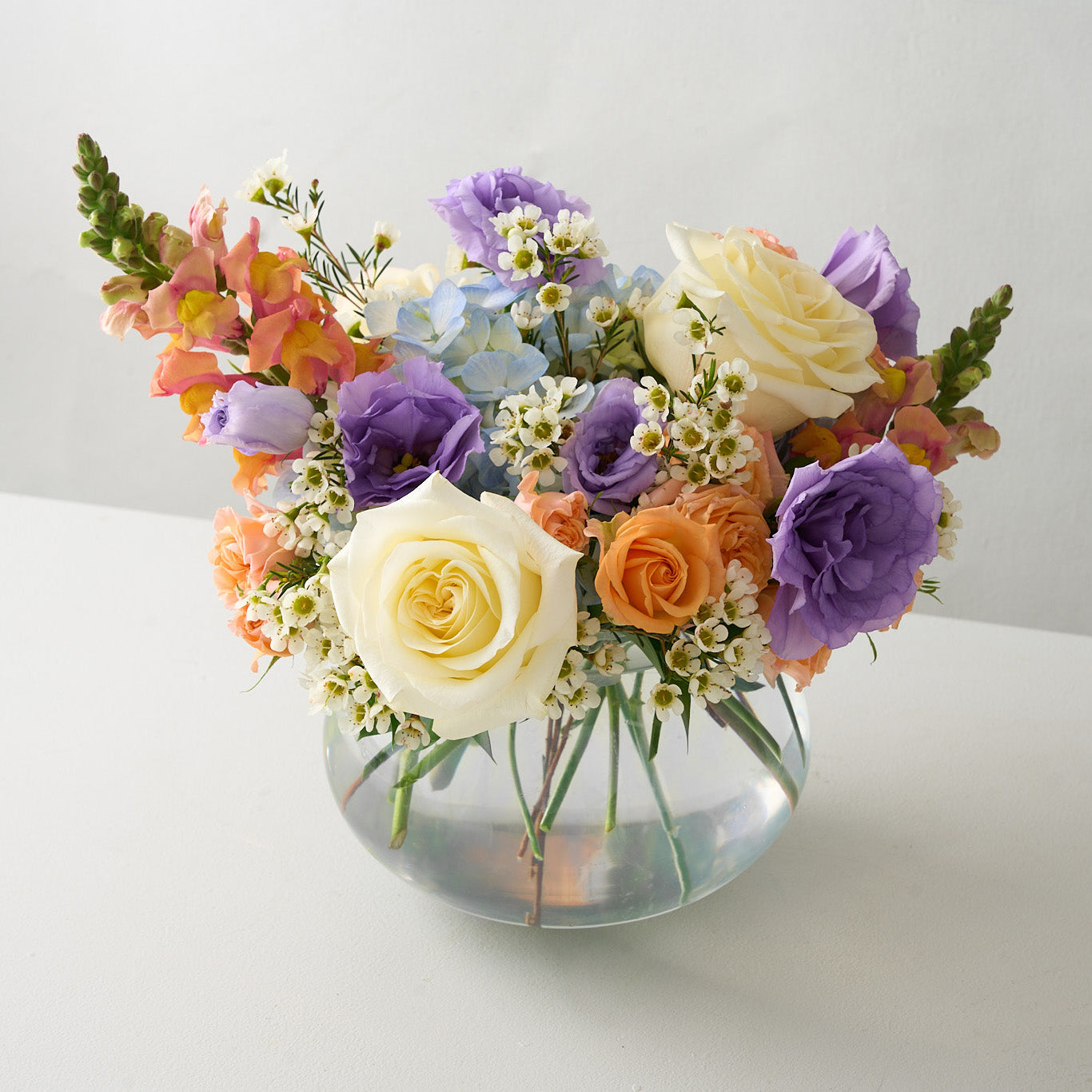 Easter and passover arrangement with peach, cream, blue and purple flowers in a glass vase.