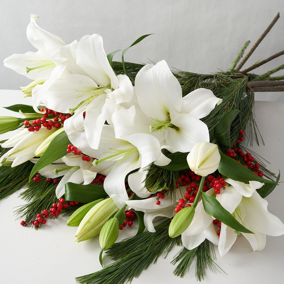 Bouquet of white lilies, red berries, and pine.