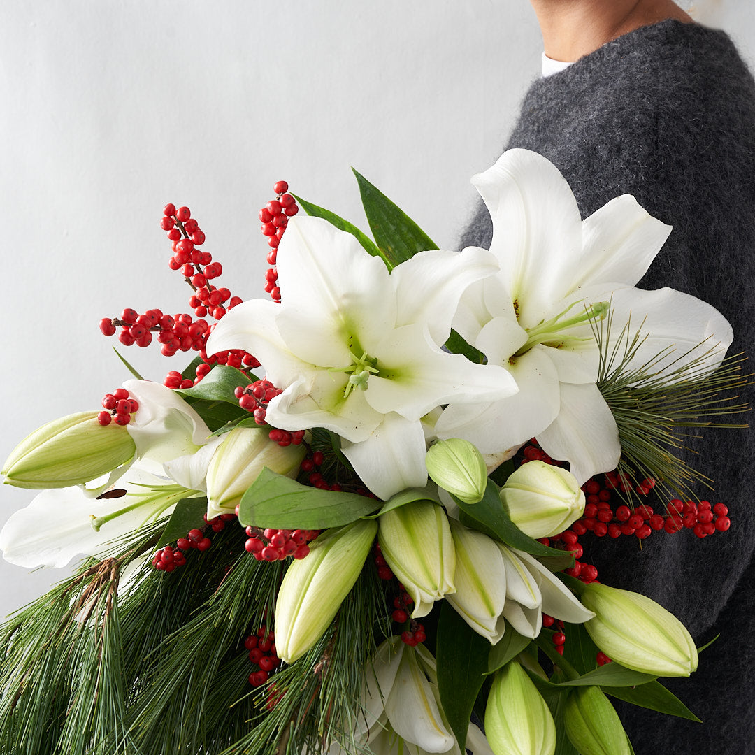 Bouquet of white lilies, red berries, and pine in persons's arms