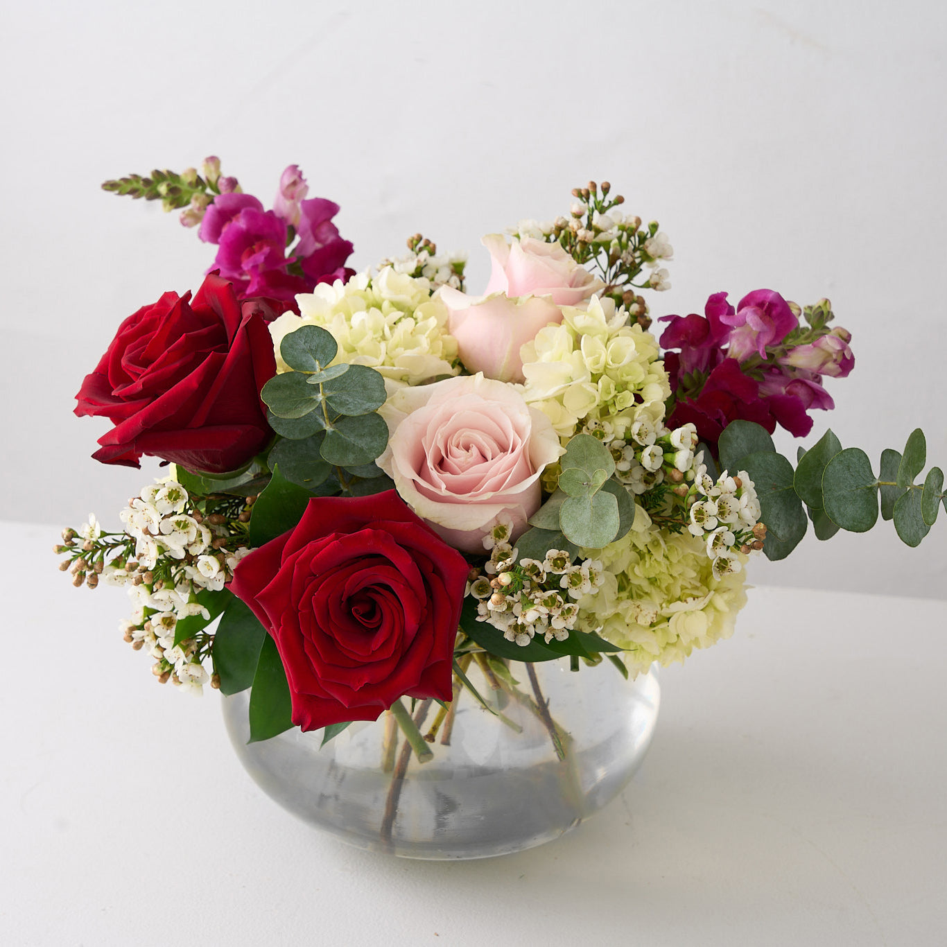 Valentine's day arrangement of deep red, & soft pink roses with hot pink snapdragons in a small round, clear vase.