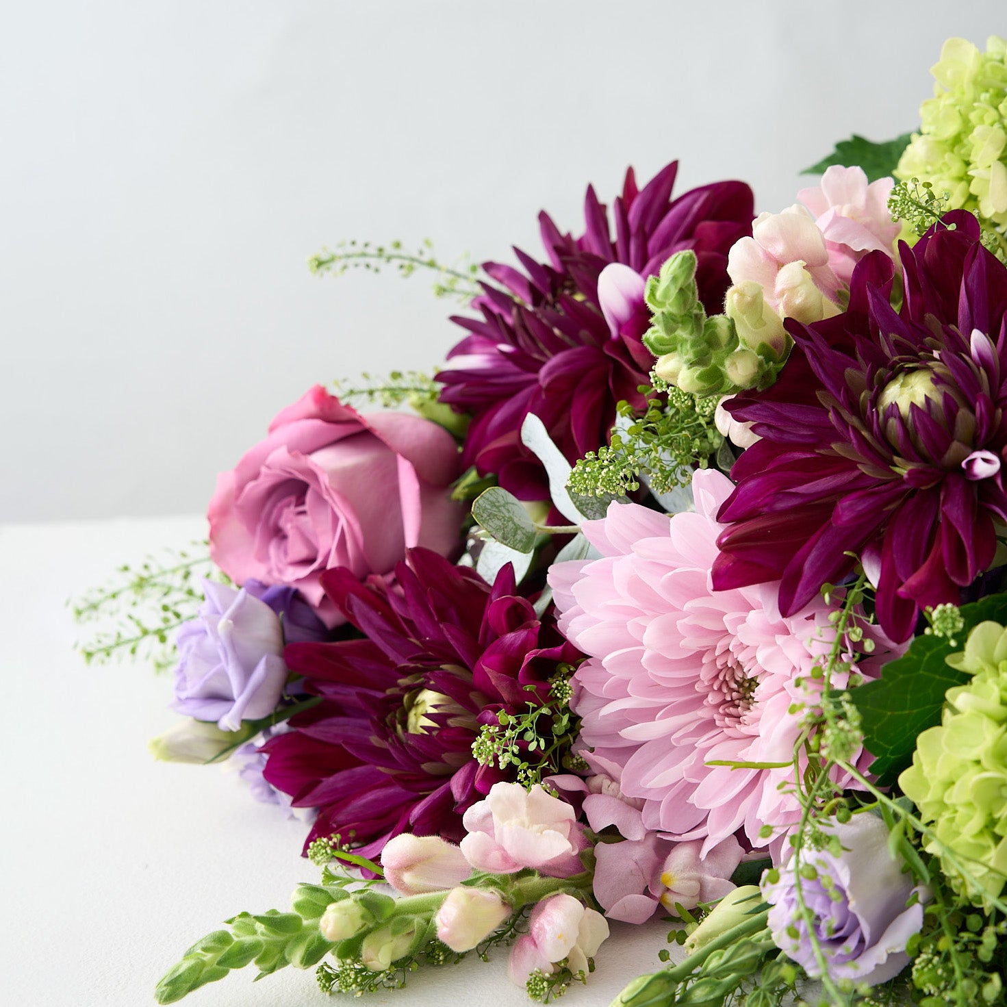 Bouquet of purple, pink dahlias, mauve long stemmed roses green hydrangea and lavender Lisianthus on a light gray background