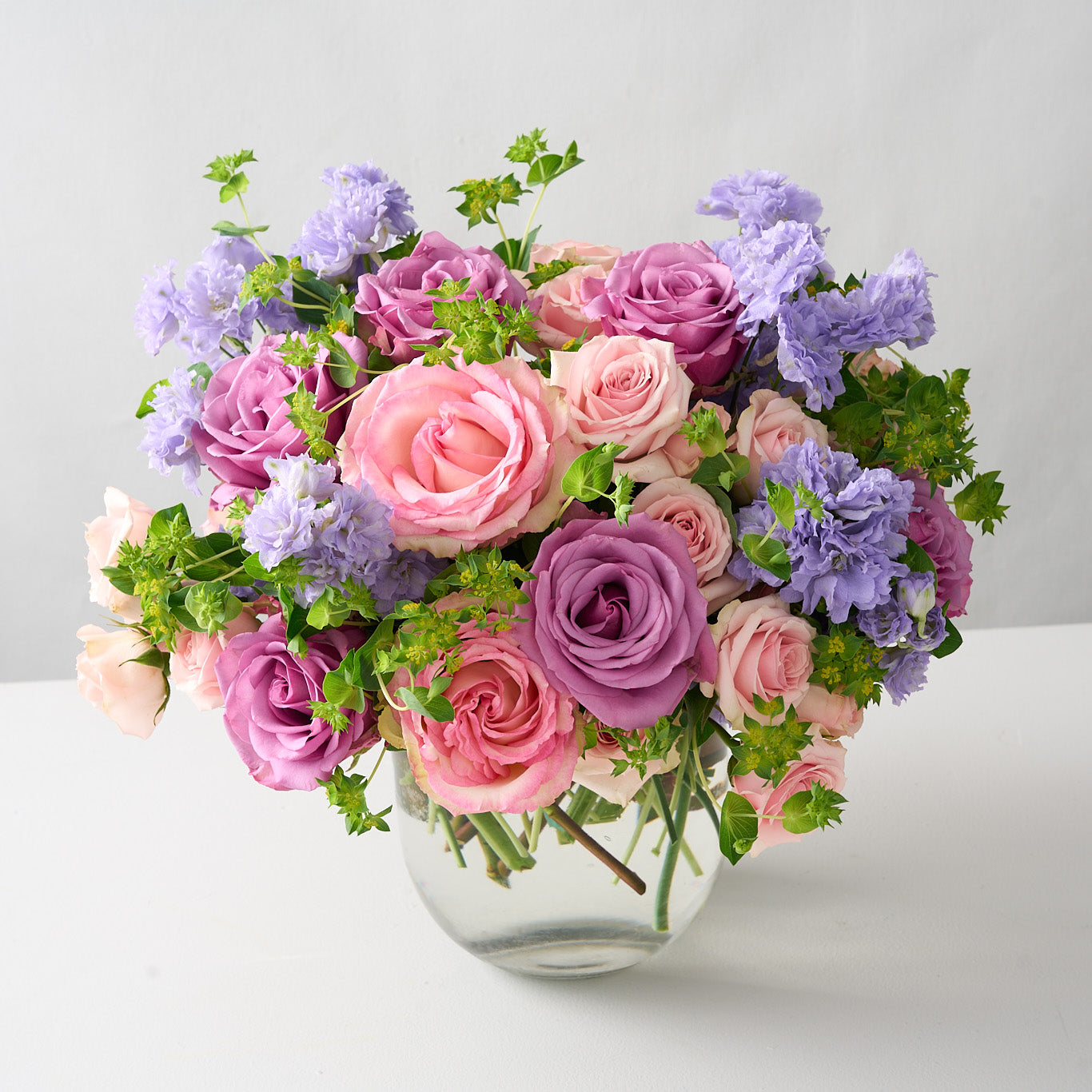 soft pink spray roses, green Bupleurum, lavender delphinium, Piacere roses, and Esperance Arranged in a round-bottom vase
