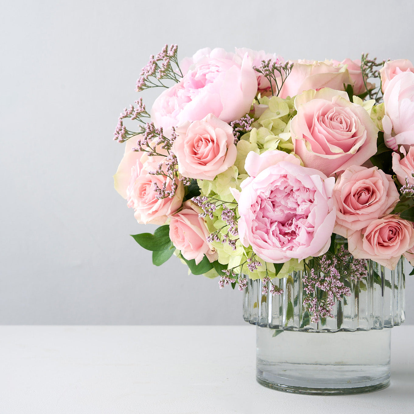 Glass vase with pink peonies, pink roses, green hydrangea, baby's breath and some greenery