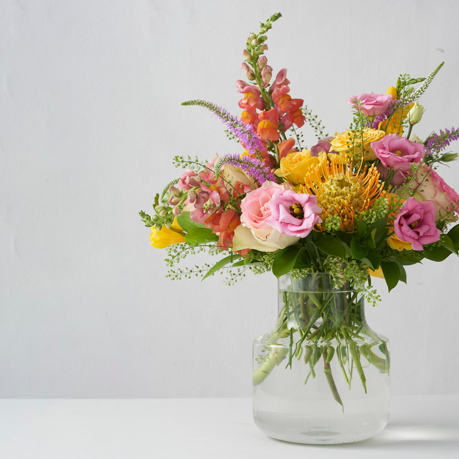 Yellow and pink flowers, arranged in clear glass vase, on white background.