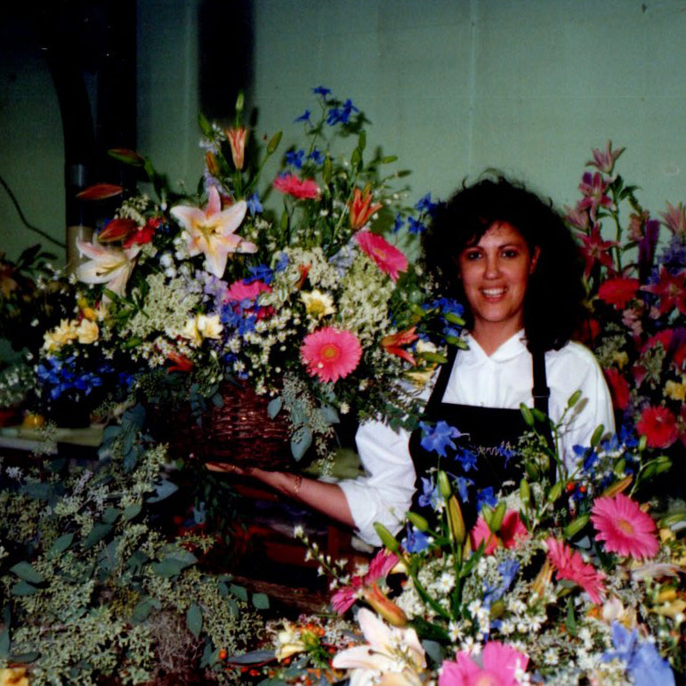 Smiling woman with dark hair, surrounded by colourful flower arrangements.