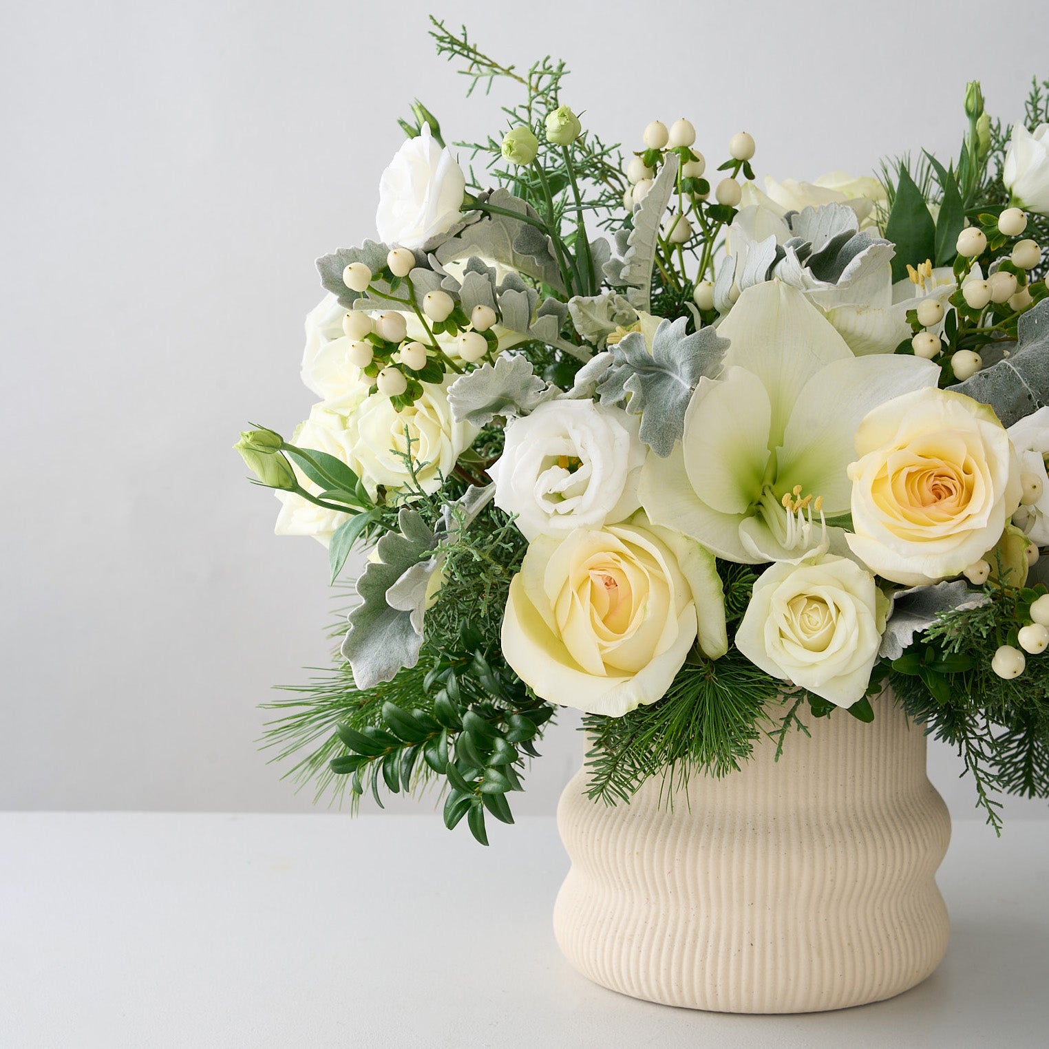 Christmas flower arrangement with white cymbidium orchid, white roses, lianthus, hypericum with silver green leaves, boxwood and other winter greens.