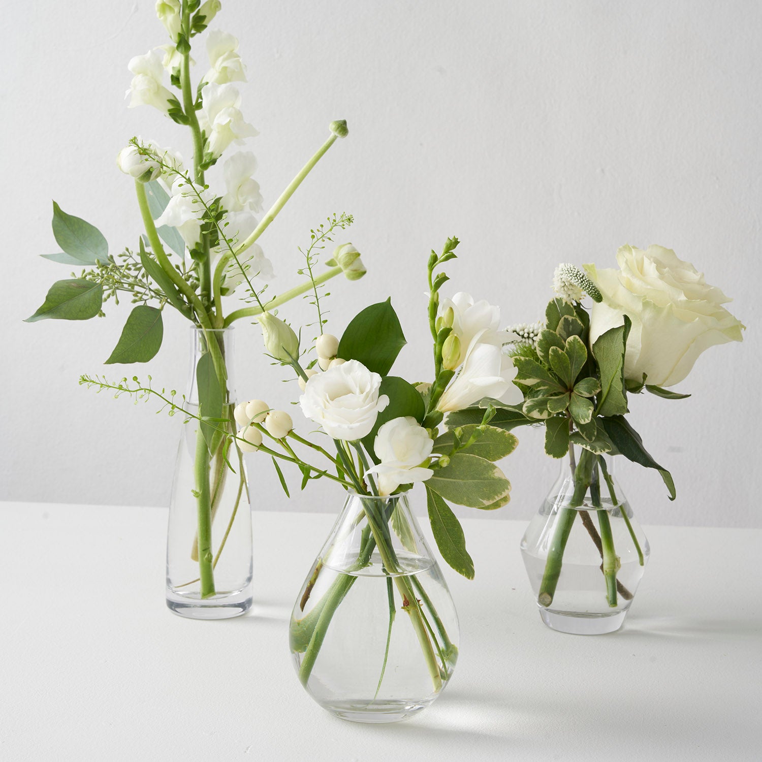 Three small bud vases filled with small white flowers on white background.