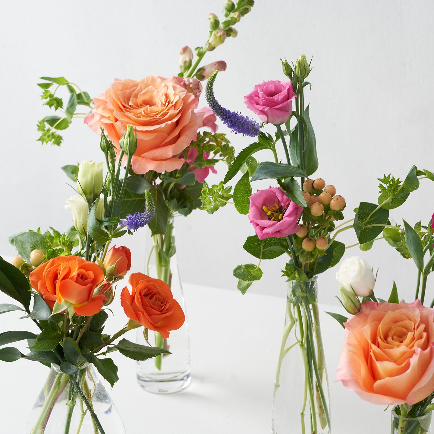 Closeup of orange, pink, and purple flowers in small glass vases on white background. 