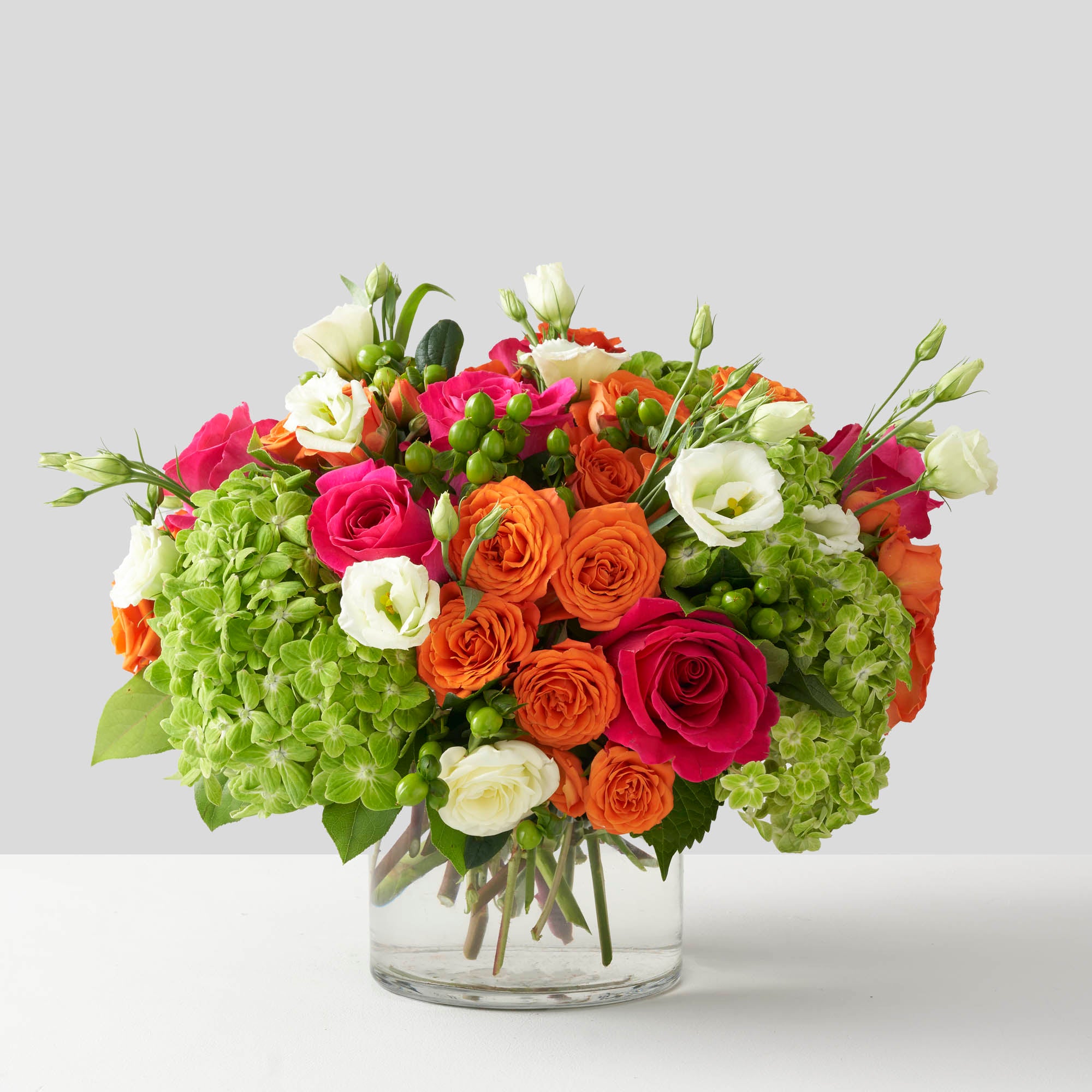 Hot pink, orange, lime green and white, flowers arranged in simple glass vase on white background.