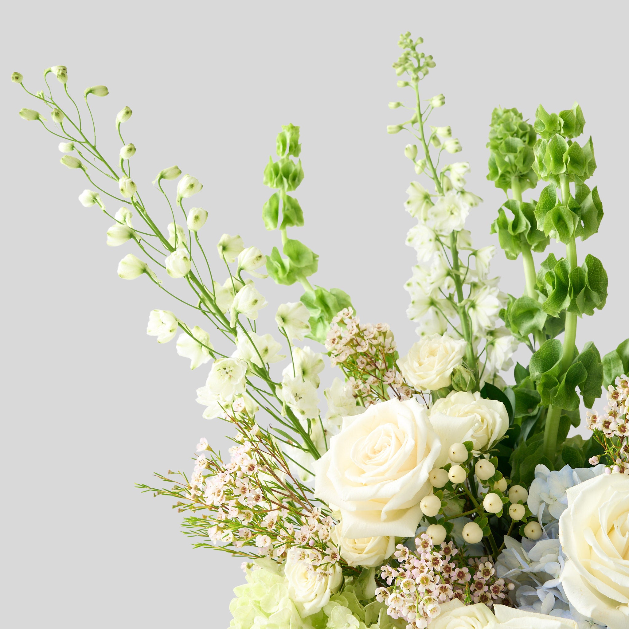 Up close photo of white delphinium, green bells of Ireland, blue & green hydrangea, cream candlelight roses
