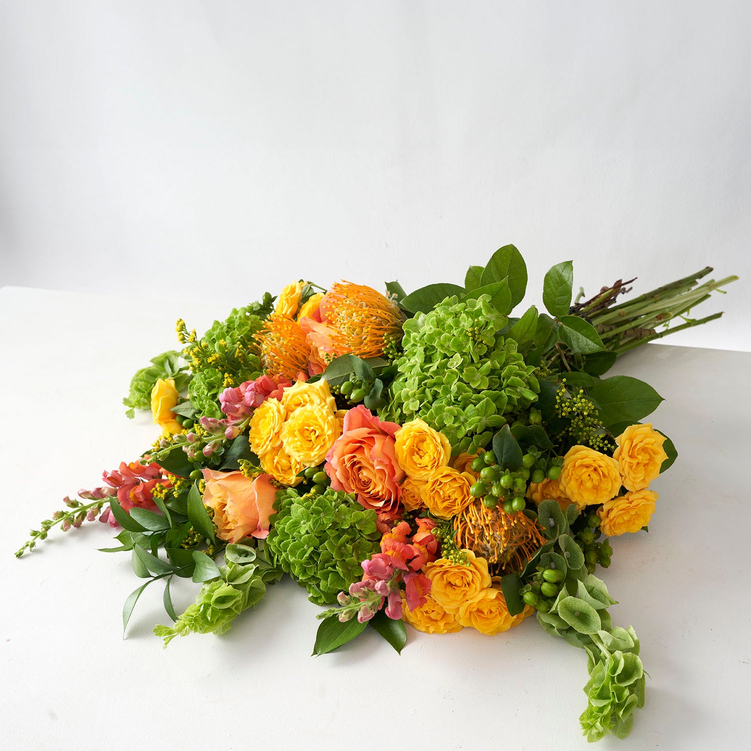Large bouquet of lime green hydrangea, orange roses yellow spray roses, and orange snapdragons on white background.