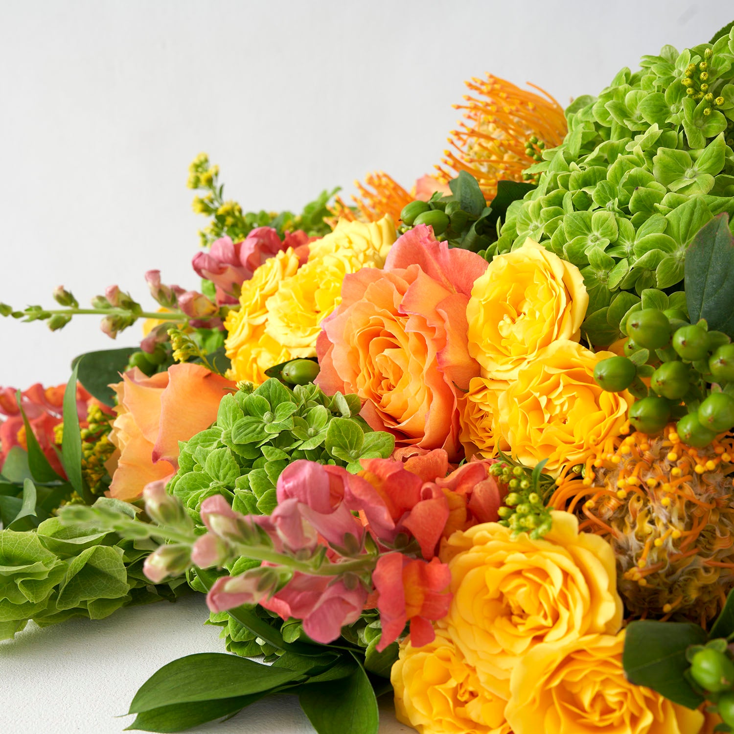 Closeup of yellow and orange roses with green hydrangea, green berries and orange snapdragons.