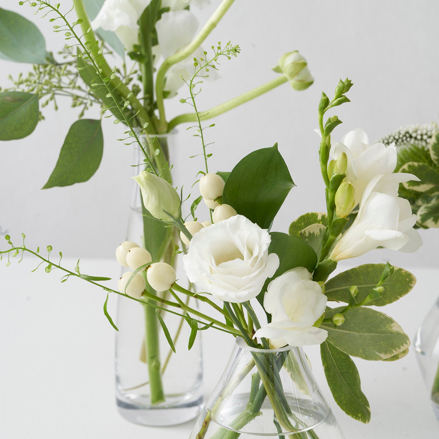 Closeup of small glasse vases with white and green flowers on white background