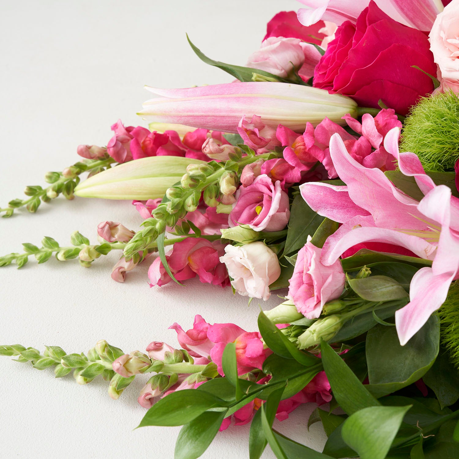 Closeup of bouquet of pink lilies, pink roses, pink snapdragons and pink lisianthus.