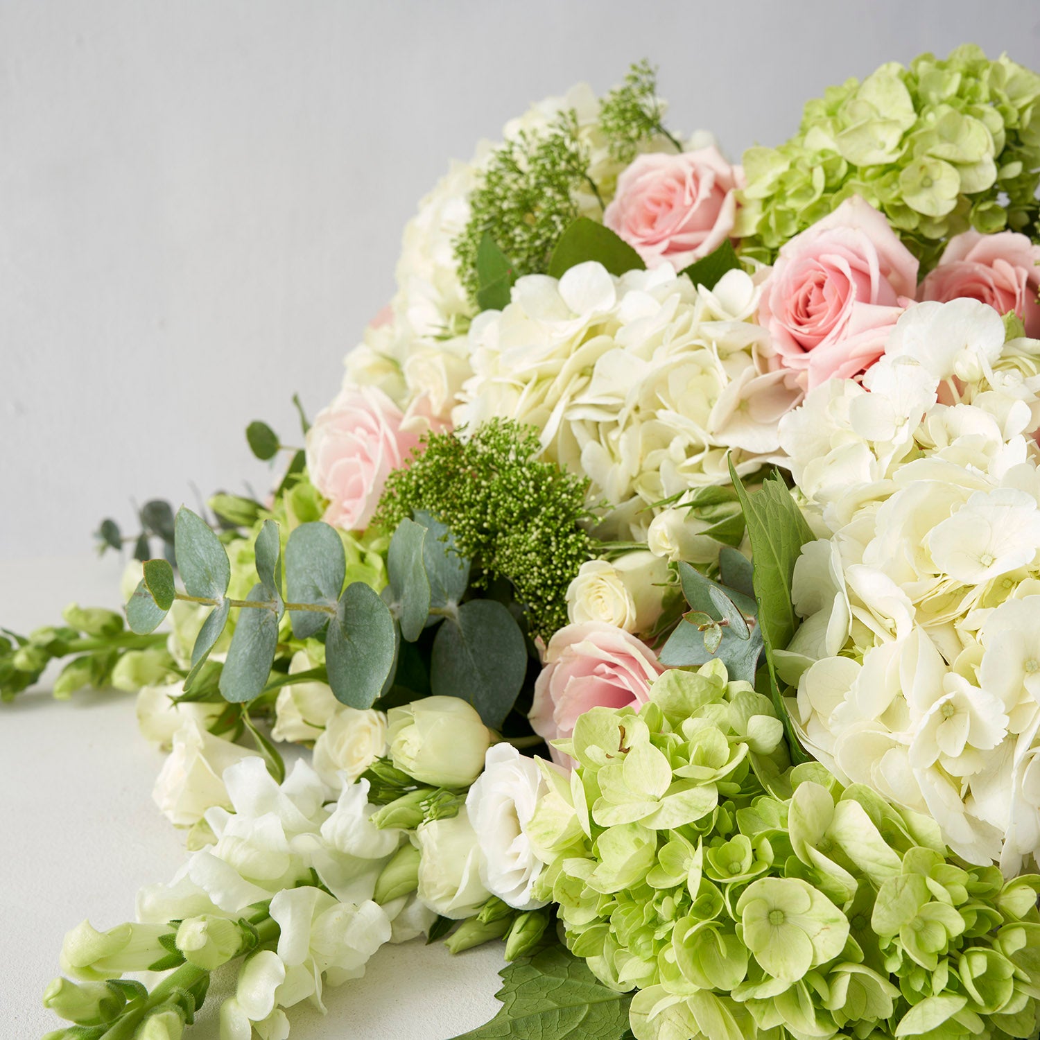 Closeup of green hydangea, white hydrangea, pink roses, Eucalyptus and a veriety of other flowers.