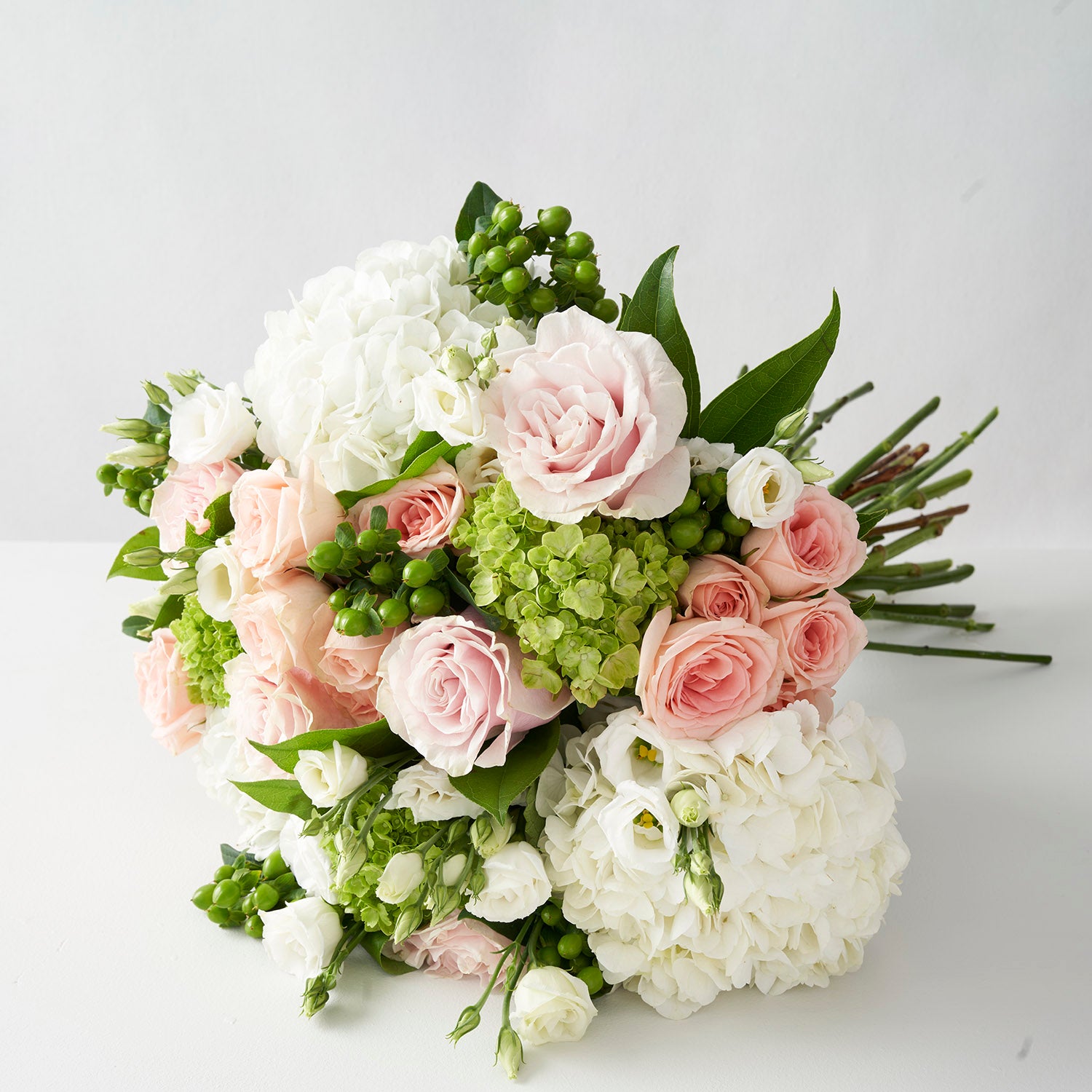 Round tradional style handtied bouquet in pinks whites and greens, including roses, hydangea and lisianthus on white background.