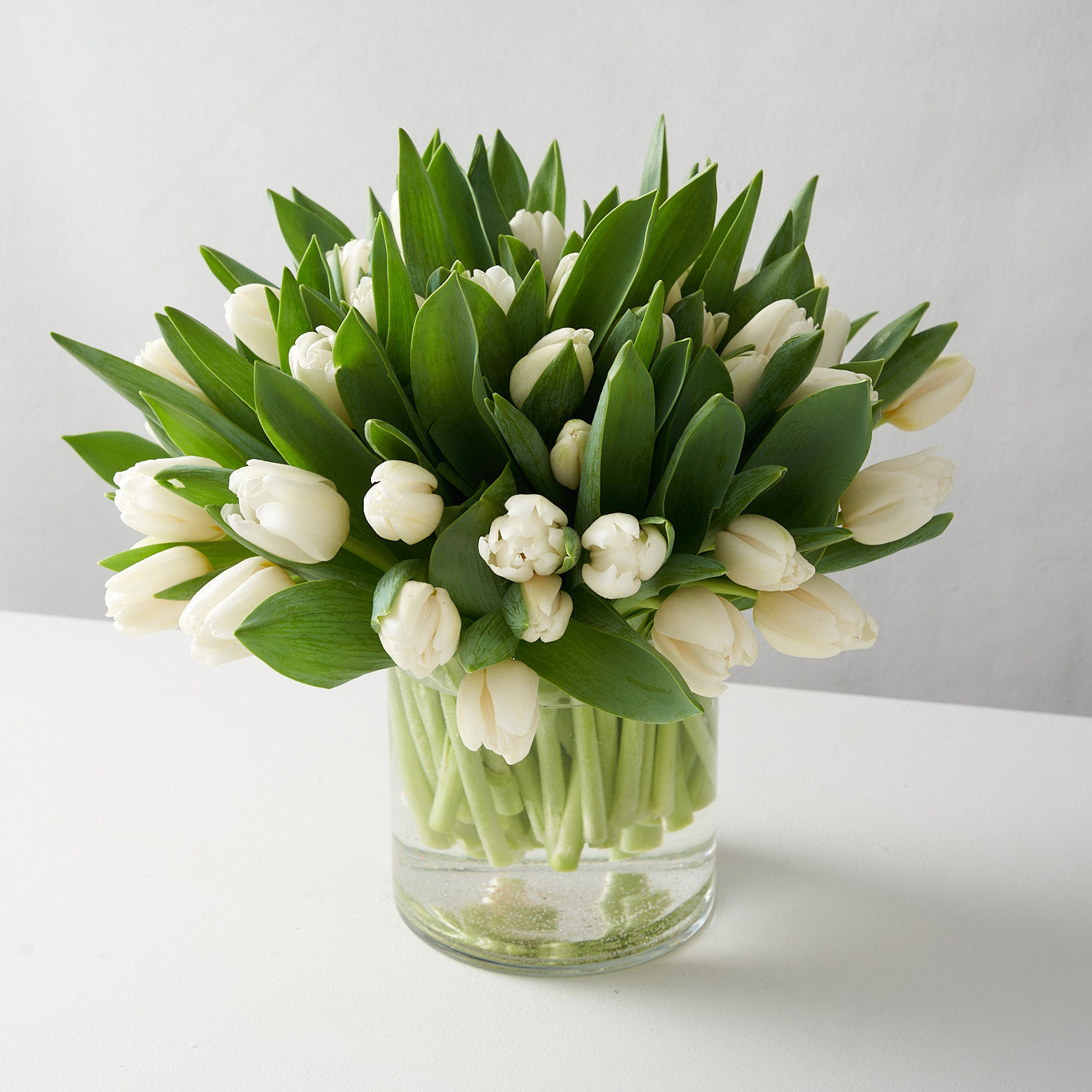 Cylindrical clear glass vase filled with white lilies