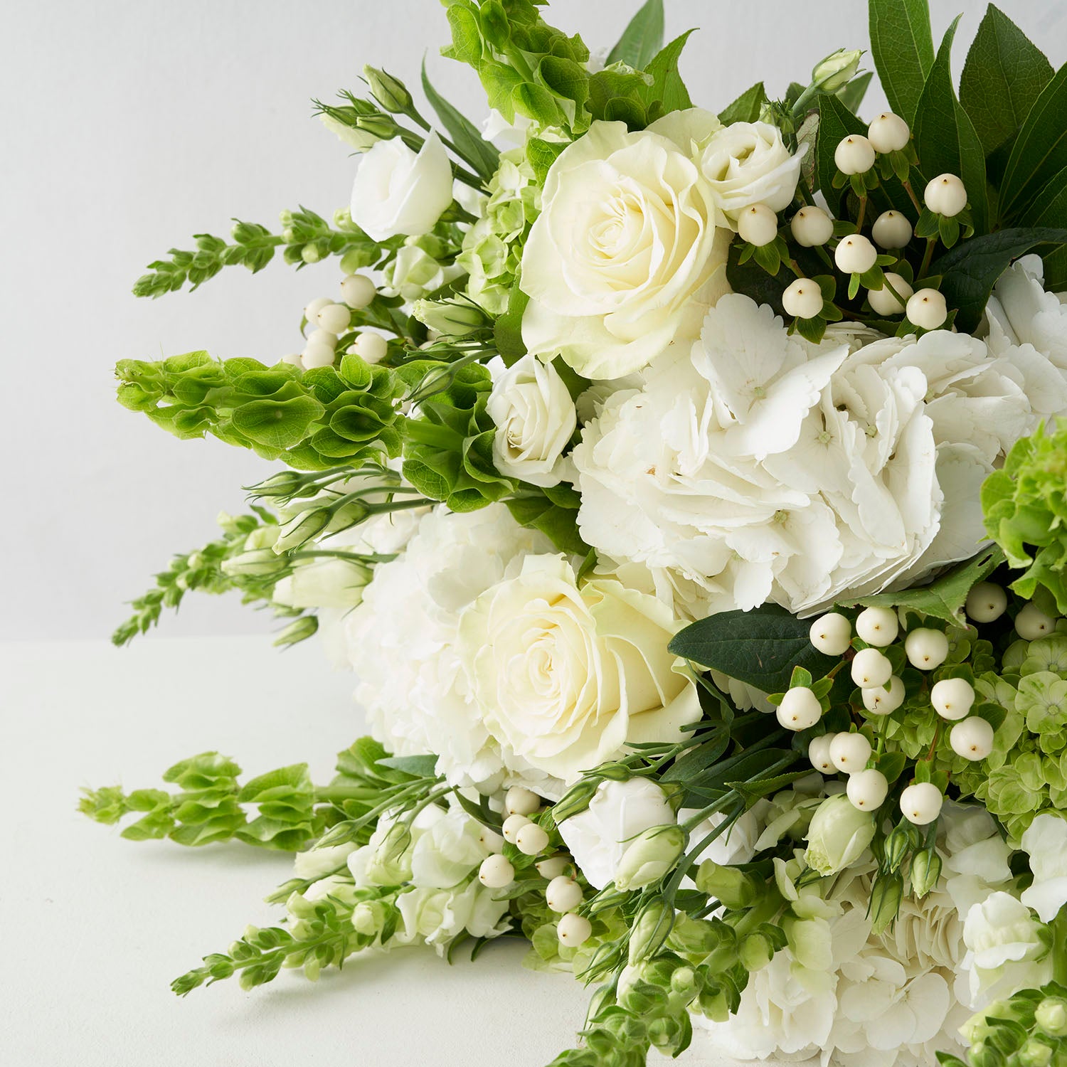  Close up of white and green flowers, including roses, hypericum berries, hydrangeas, snapdragons, and bells of ireland.