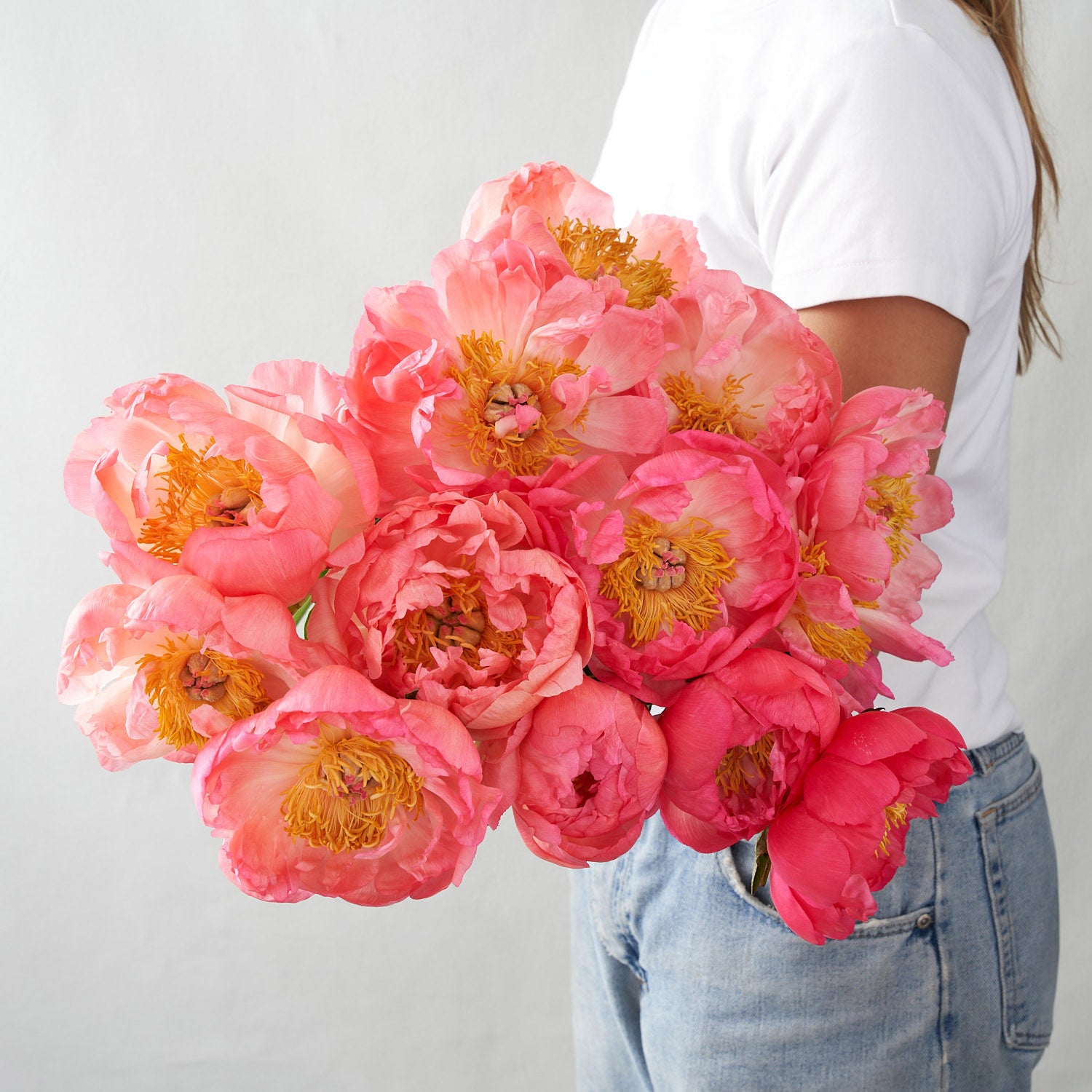 Woman in white holding a bouquet of coral sunset peonies