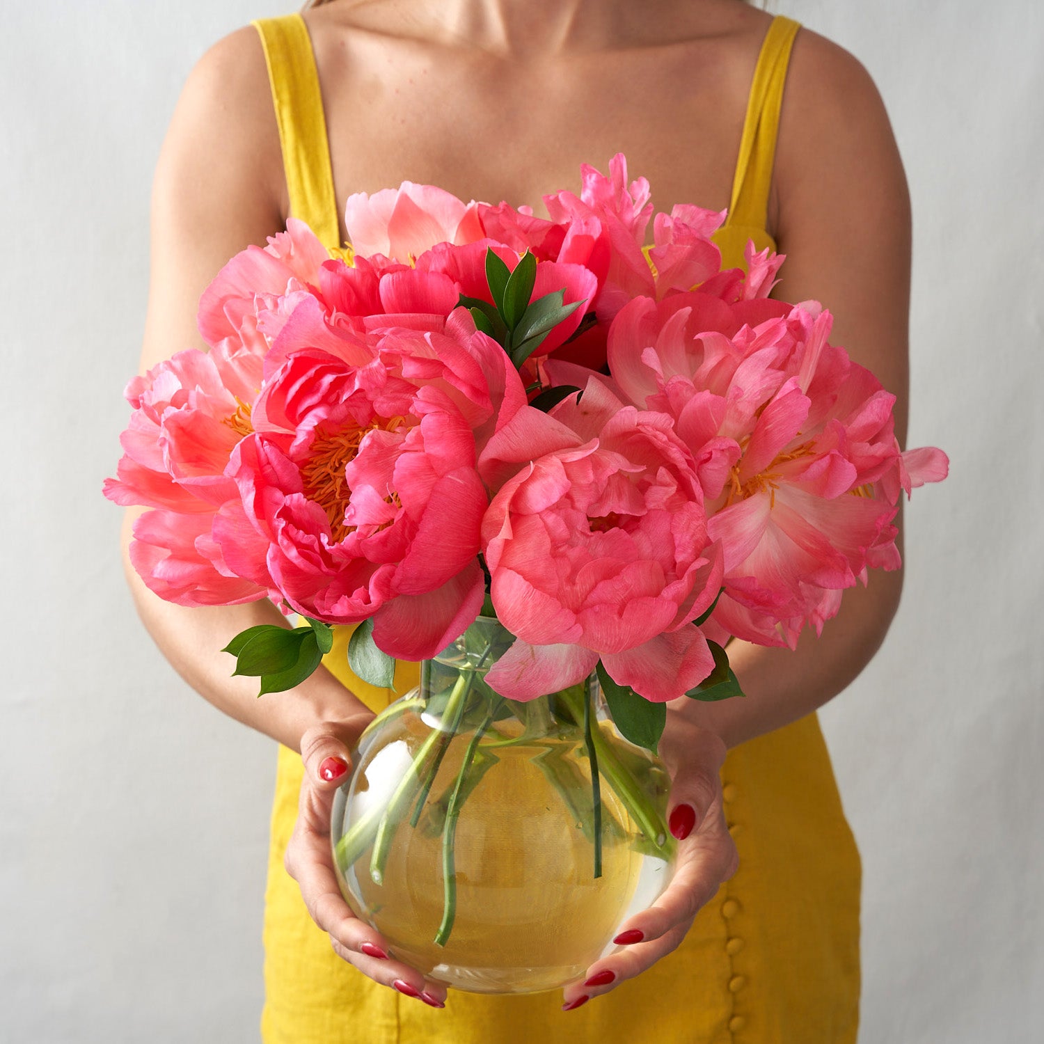 Woman in yellow holding round vase with coral peonies and greenery