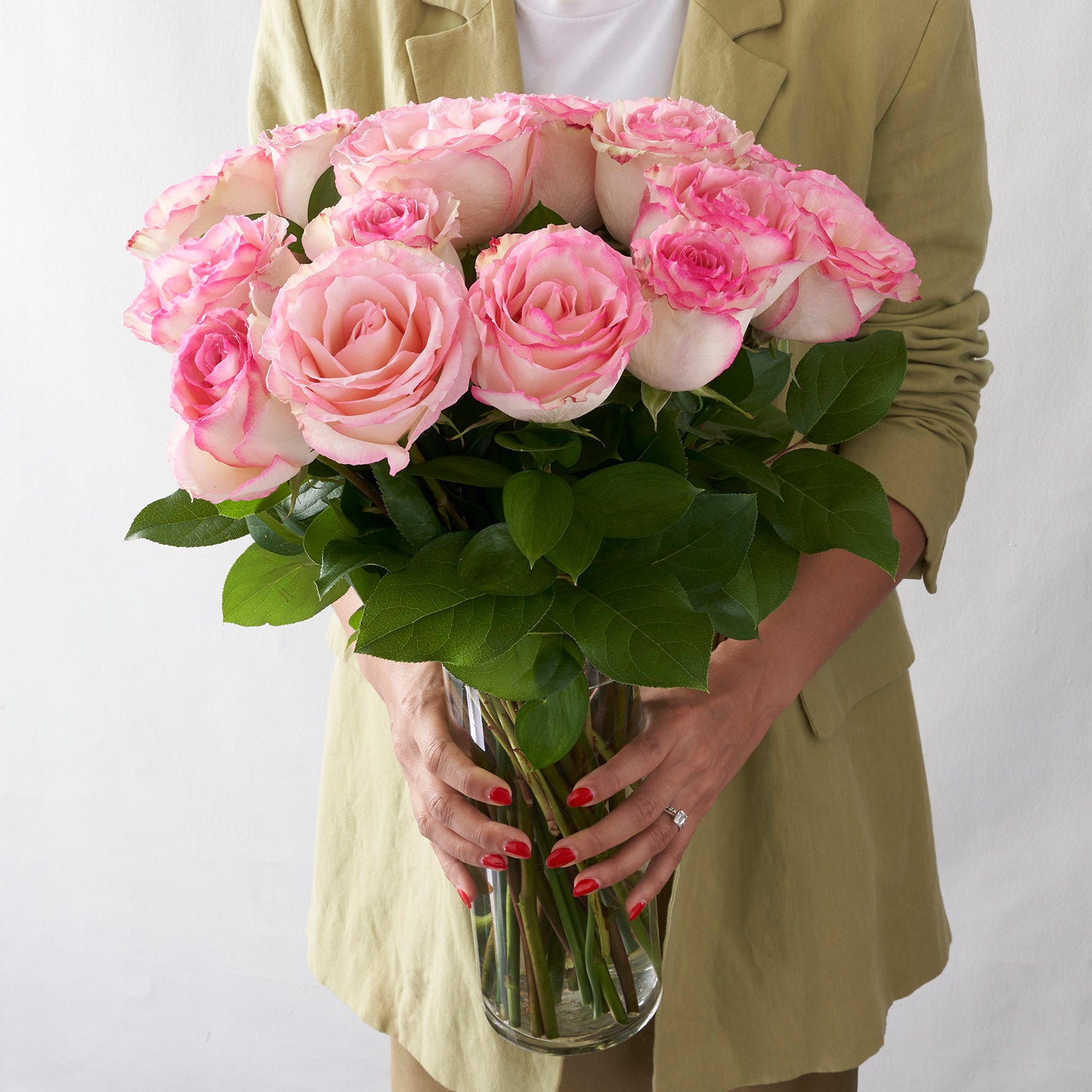 woman in pale green coat holding glass vase full of pink Esperance roses.
