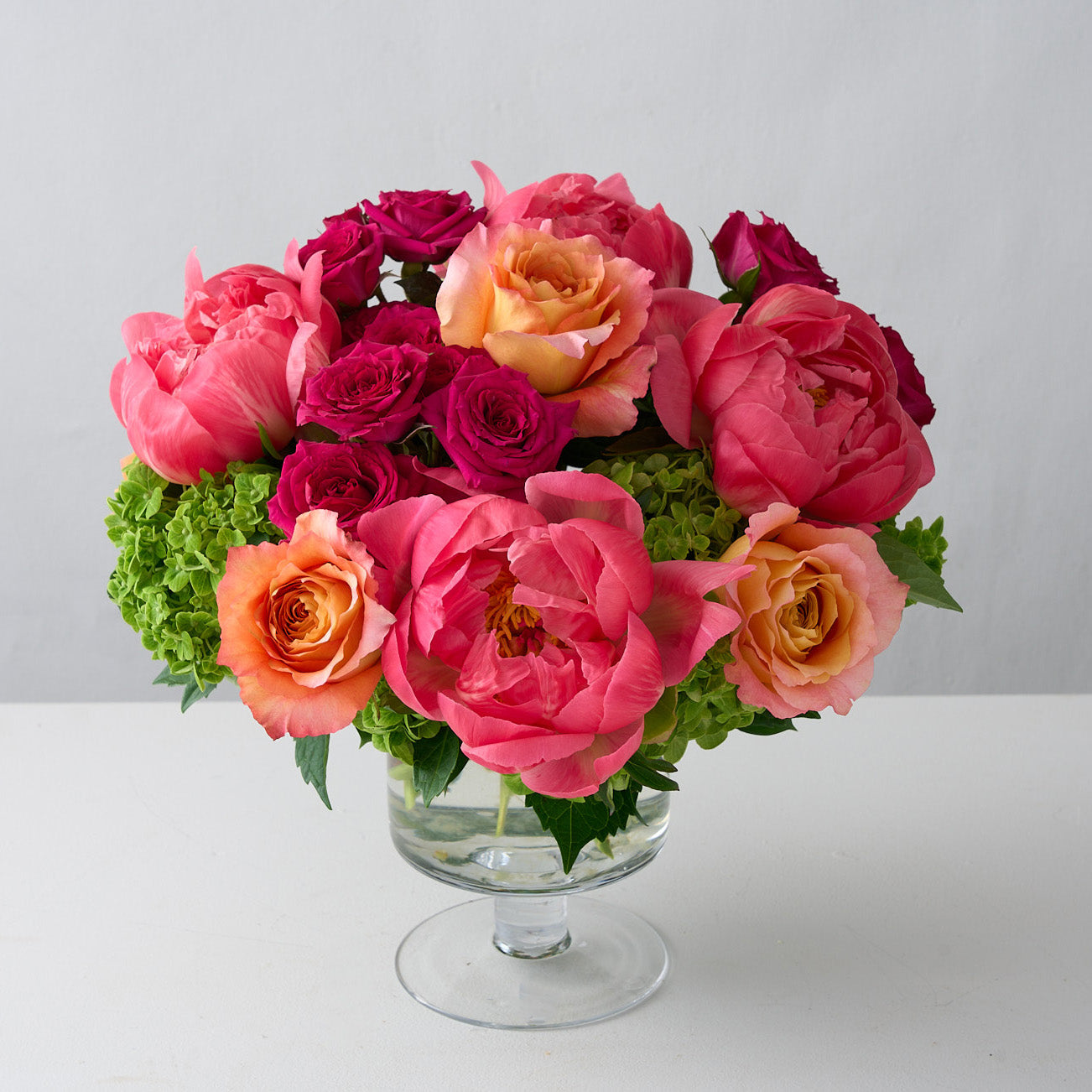 A glass vase filled with pink peonies, orange and pink roses, and green hydrangeas, titled Eva