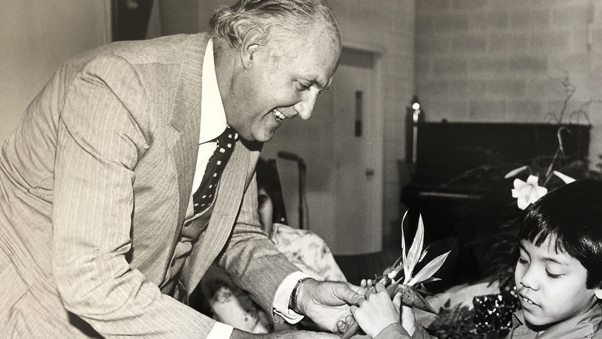 Black and white photo, of smiling man, in suit ,giving flower to a child.