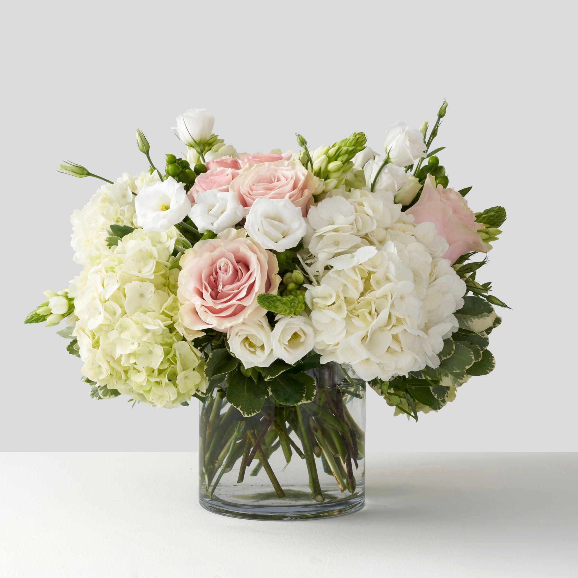 Soft pink white and green flowers arranged in glass vase on white background