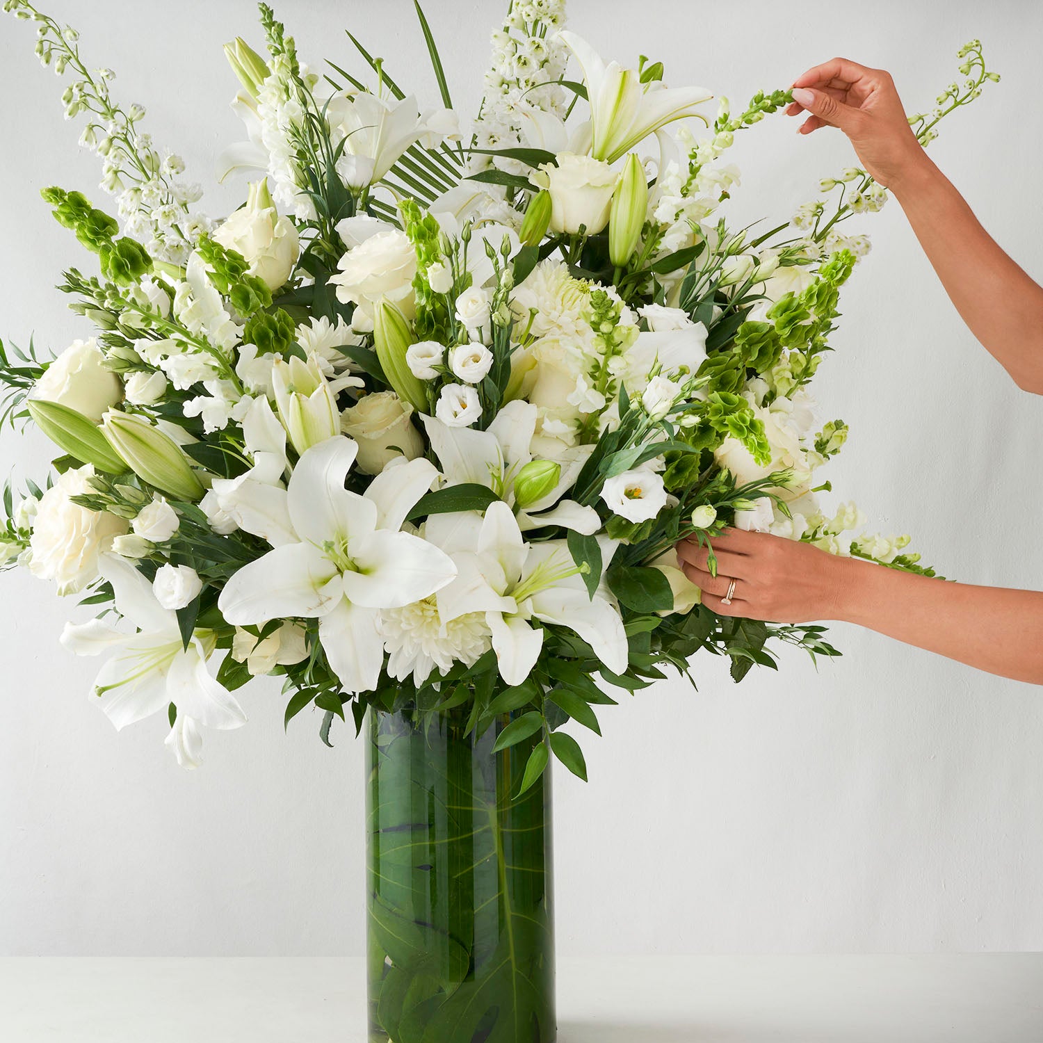 Large glass vase full of white flowers with two hands adjusting the flowers in the vase.