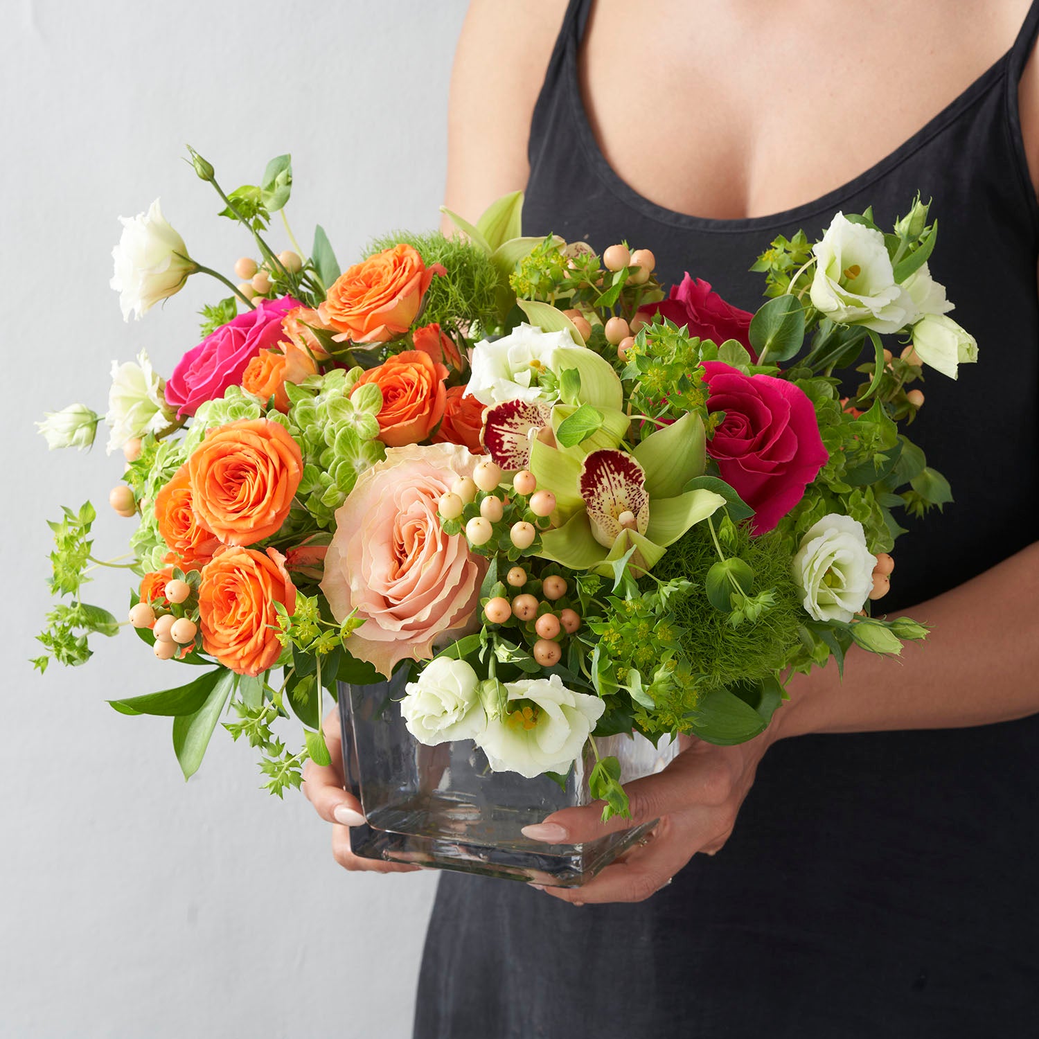 Woman in black dress holding multi coloured flower arrangement in glass vase.