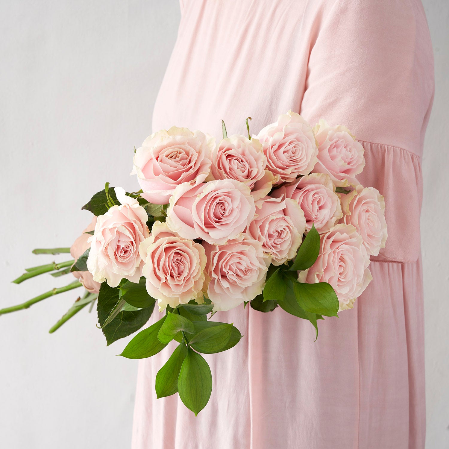 Woman in pink dress holding twelve pale pink Mondial roses.