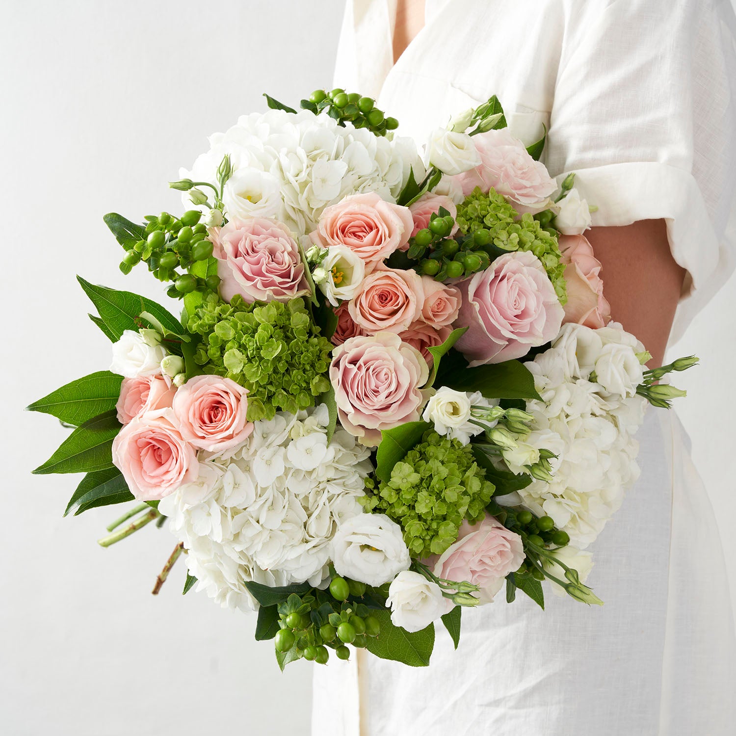 Woman in white dress holding round white,green, and soft pink, hand tied bouquet.