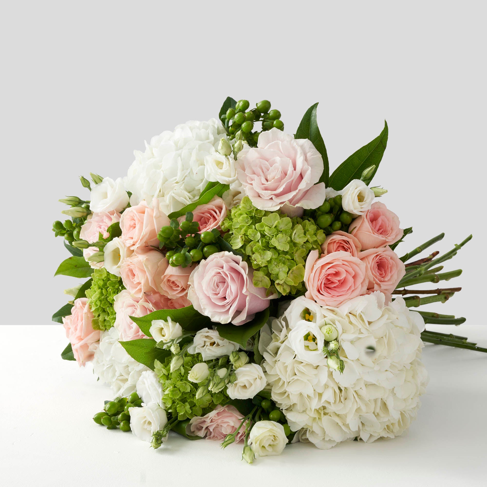 Round handtied bouquet in white, green, and soft pink, laying on white background.