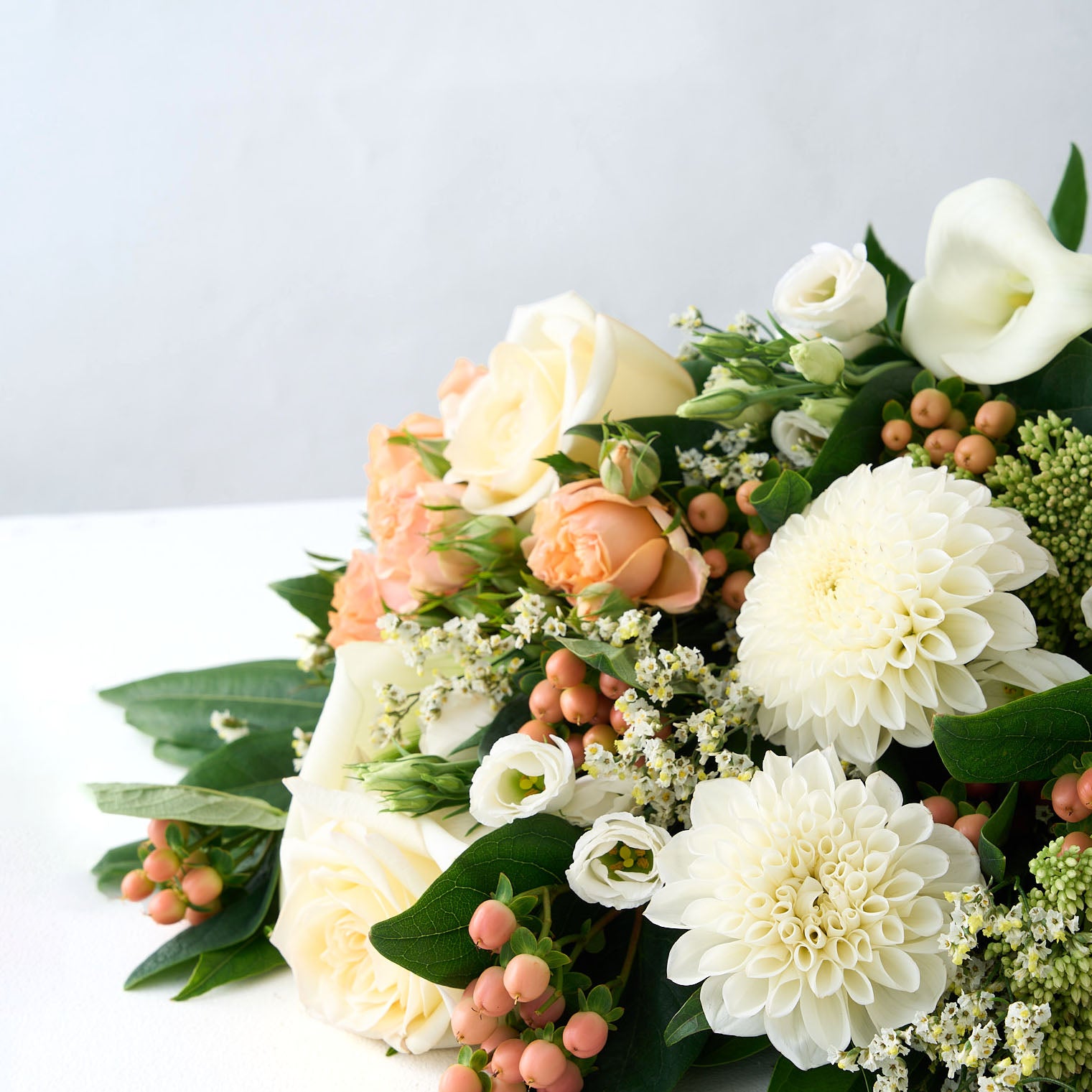 Bouquet of white pompom dahlias and Lisianthus, peach hypericum and rose with greens on a light background