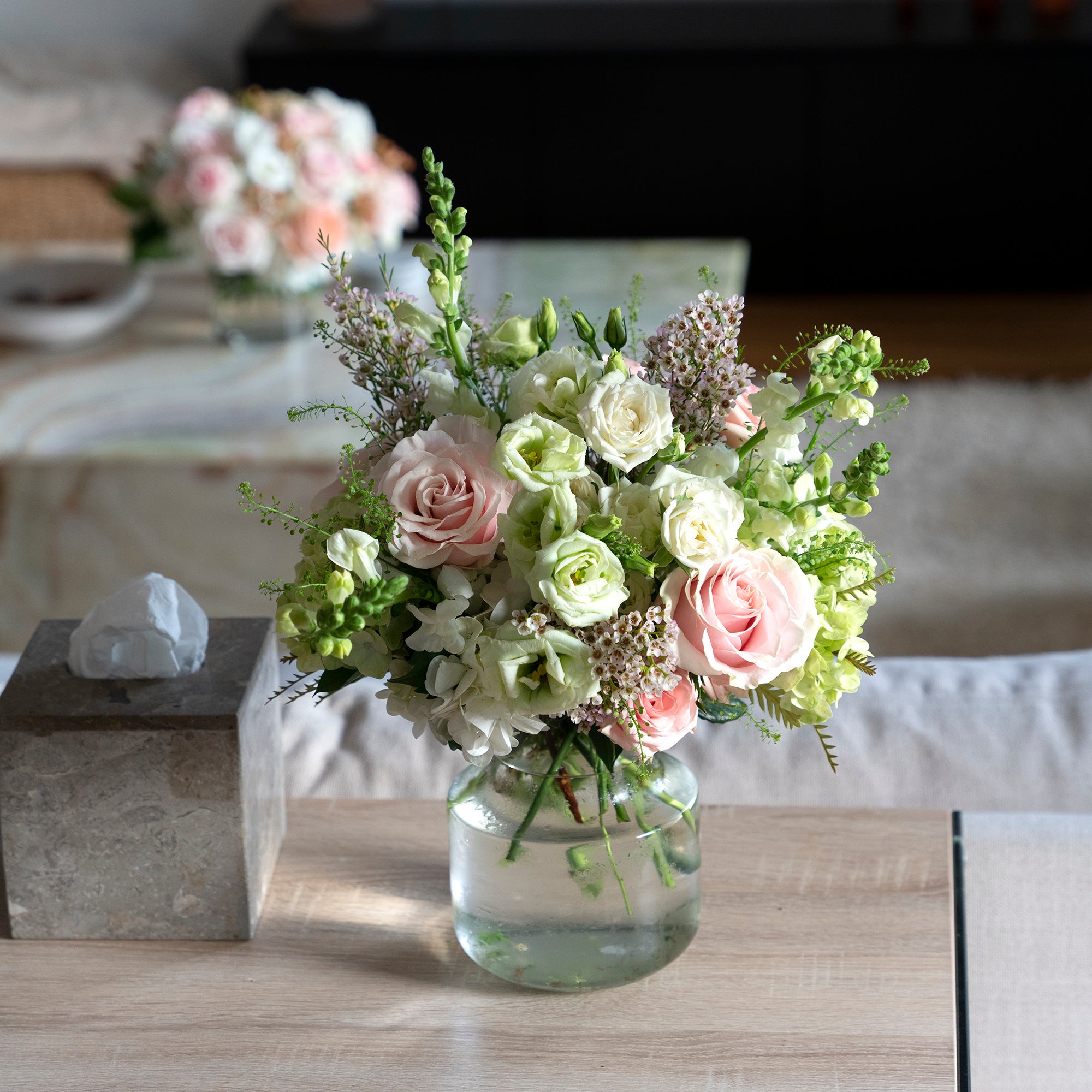 a traditional colours scheme arrangement adorned with pink oses, white lisianthus, tall snap dragons and wispy green hydrangea in a home setting