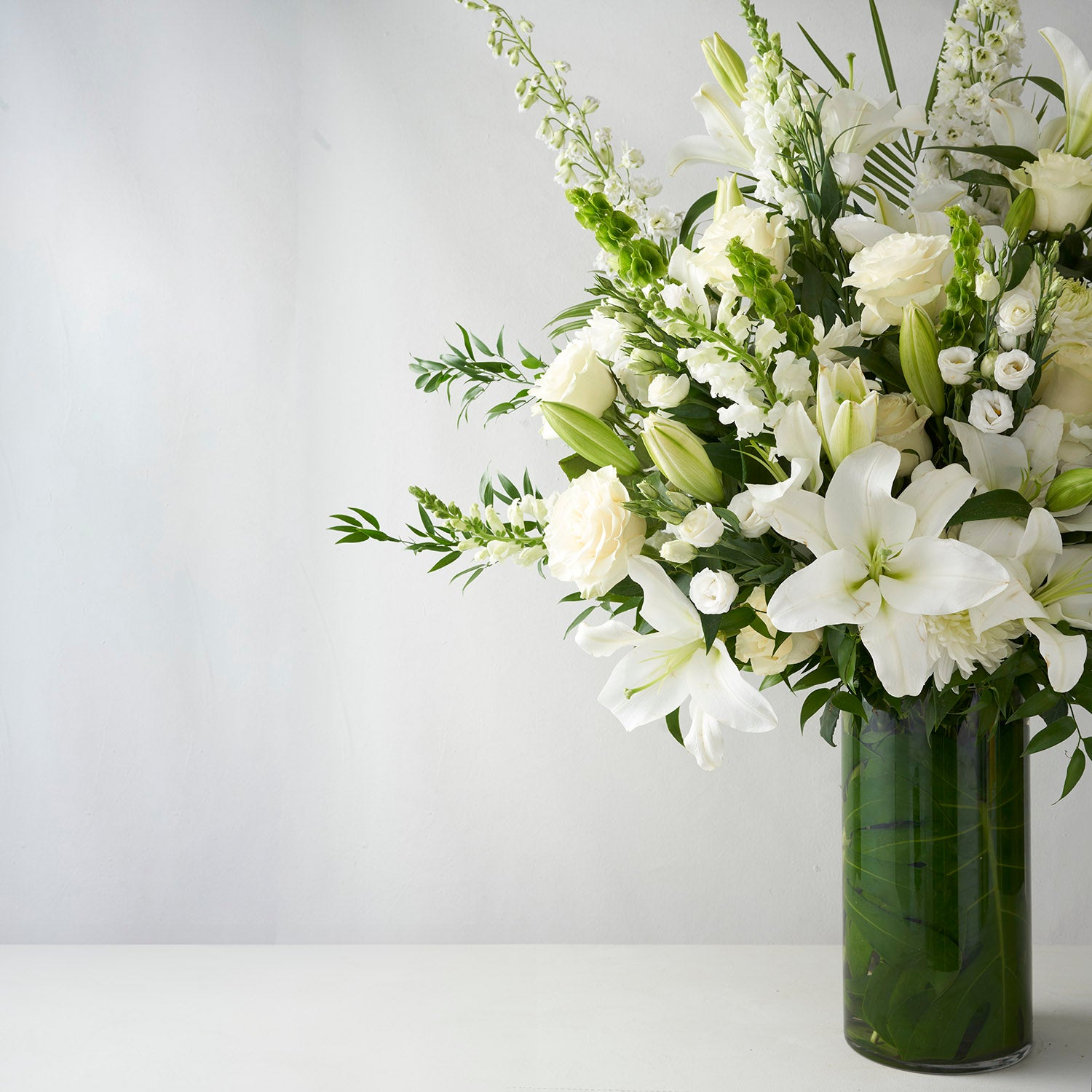Large glass vase full of white flowers including lilies. roses, snapdragons, and delphinium.