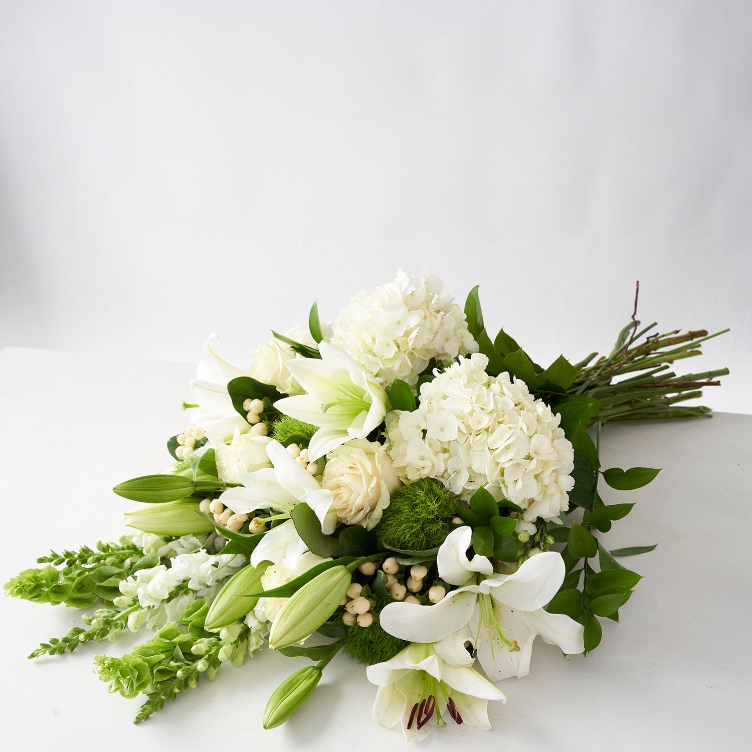 Large bouquet of white lilies, white hydrangea, cream berries and white roses on white background.