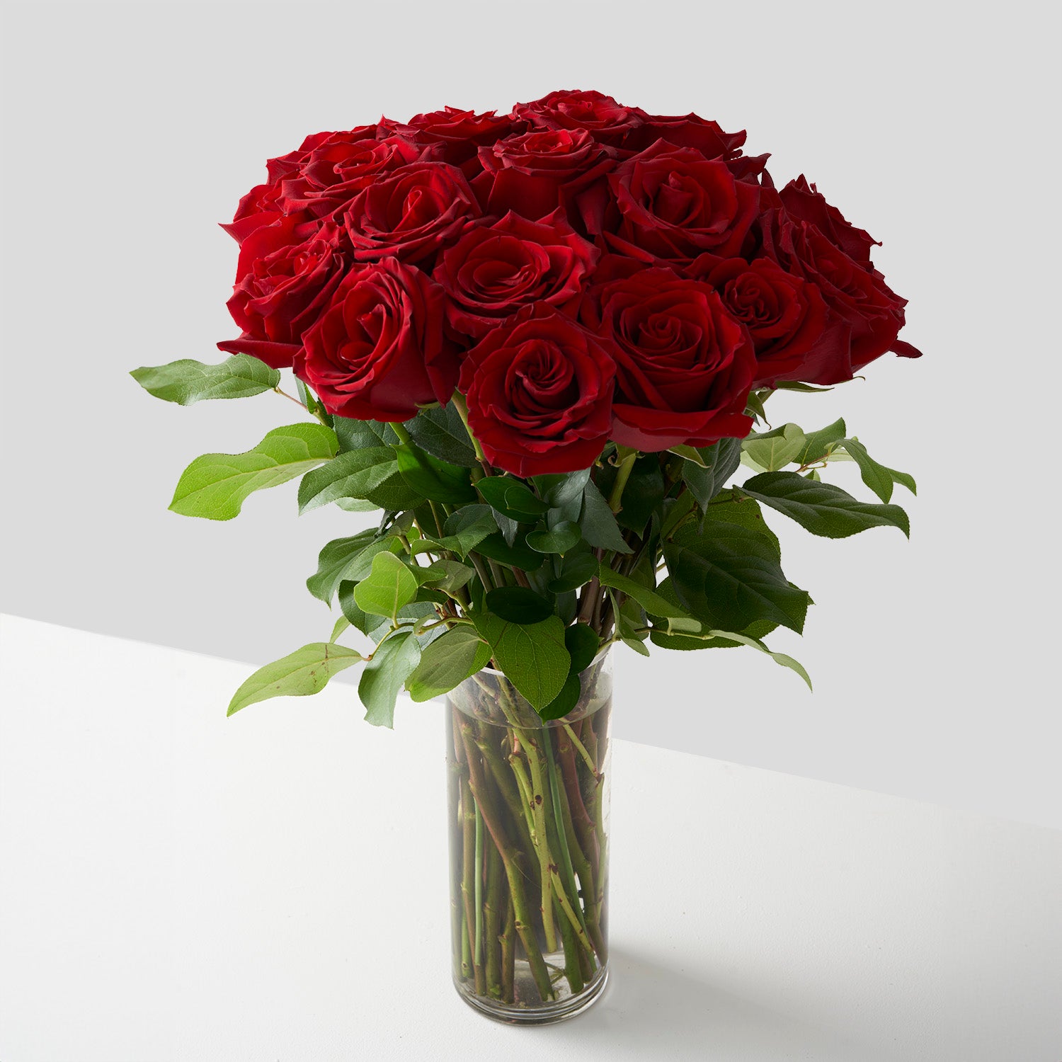 twenty-four red roses arranged with leaves in simple glass vase.