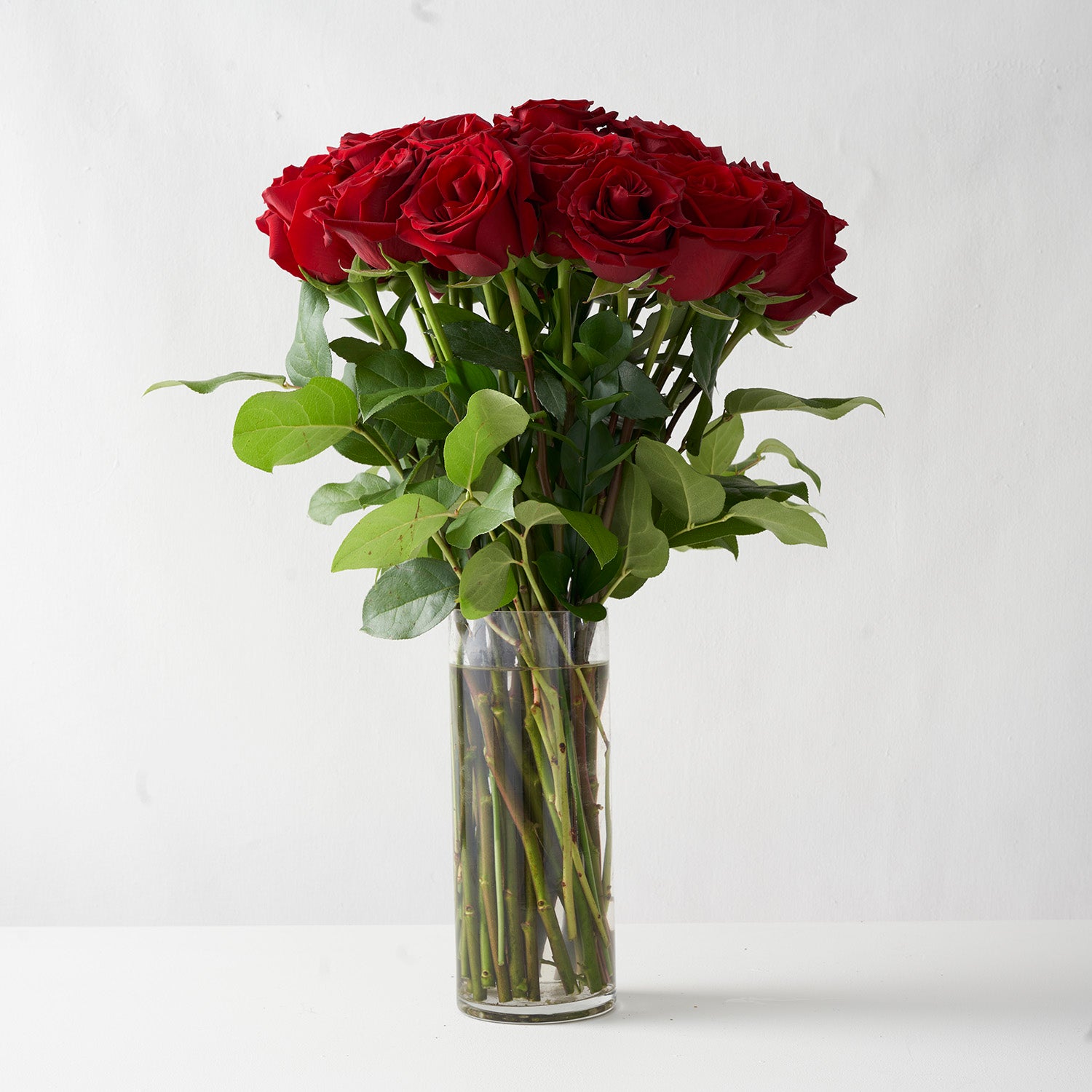 twenty-four red roses with green leaves in clear glass vase.