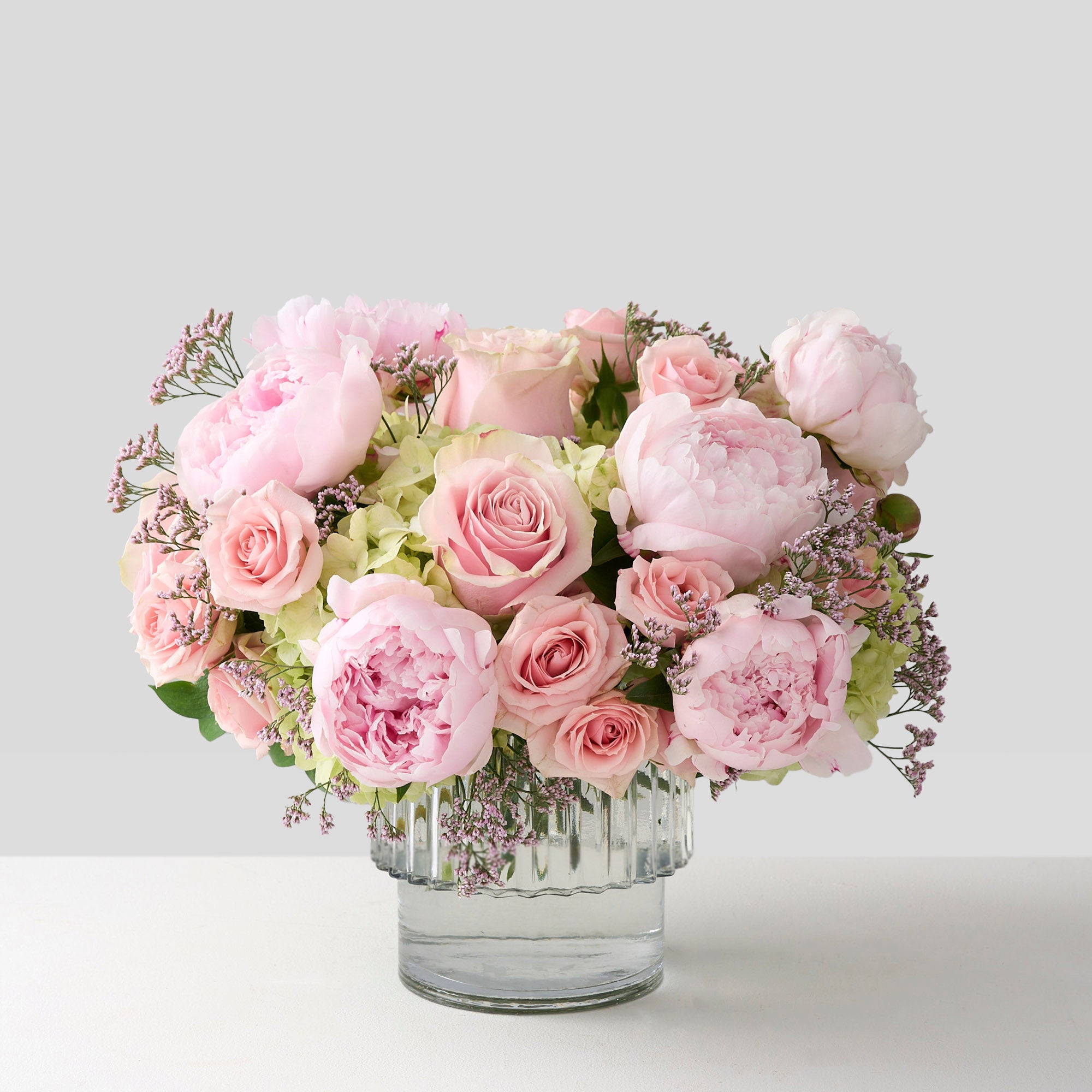 Glass vase with pink peonies, pink roses, green hydrangea and baby's breath